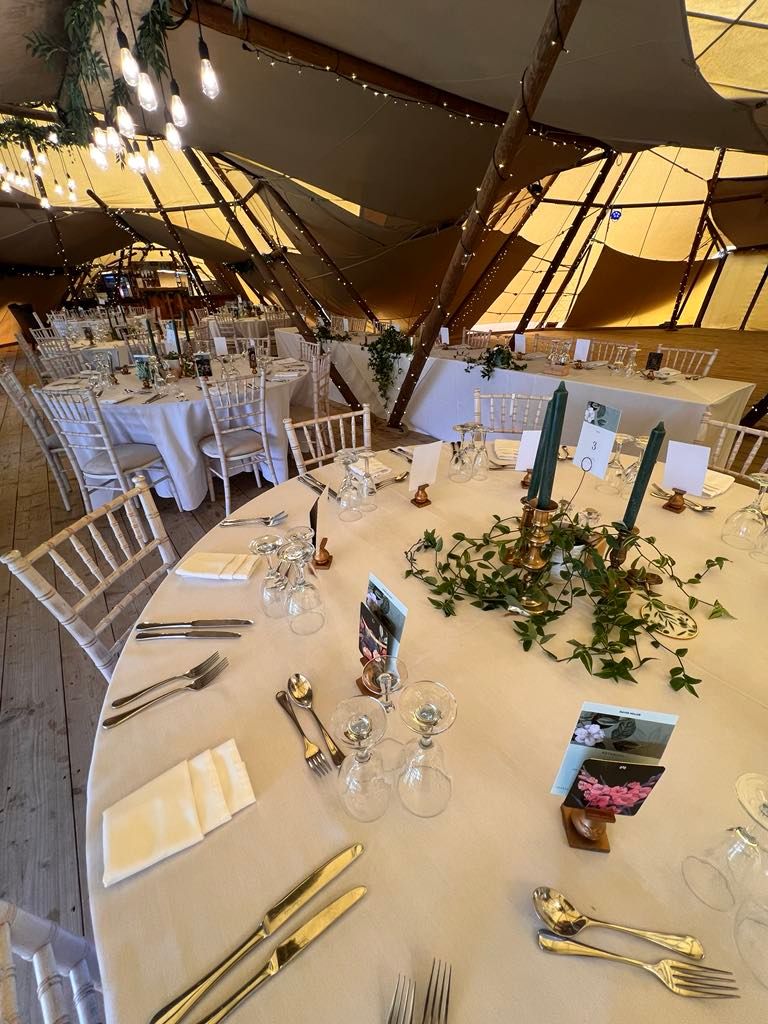 Elegant wedding reception setup with white chairs and floral centerpieces under a tent structure.