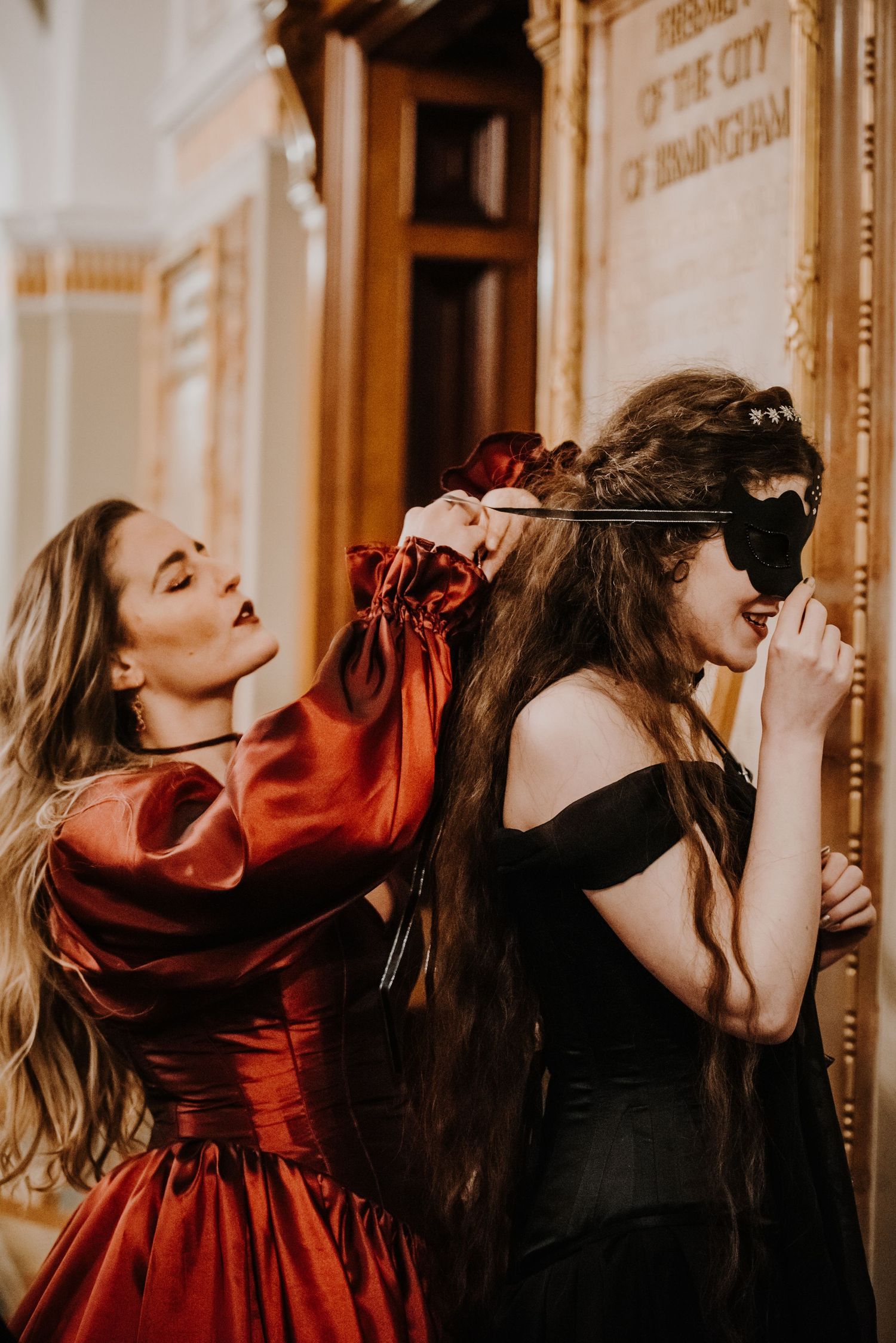 Guests in red and black formal attire dancing at masquerade ball.