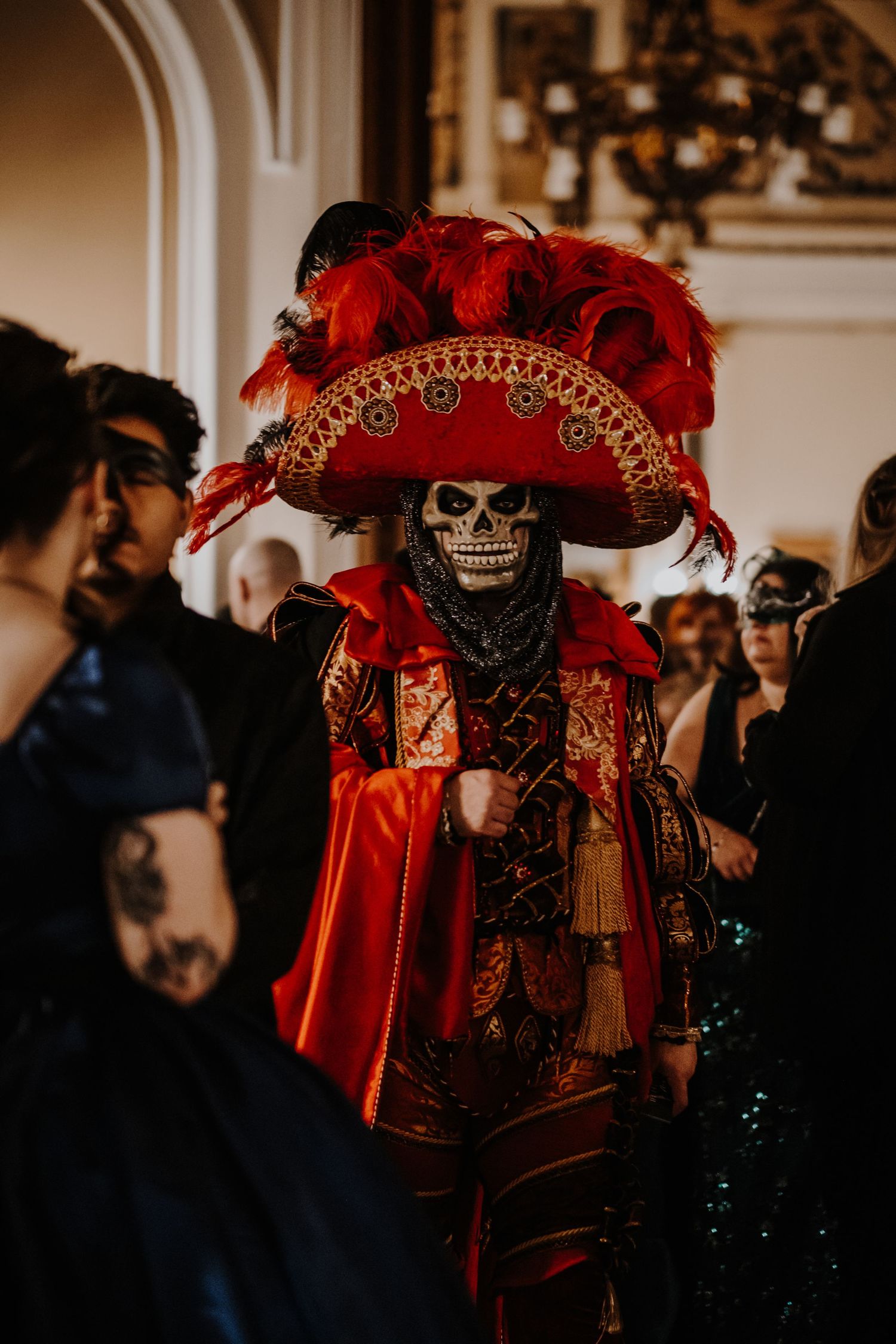 Ornate red and gold masquerade costume with feathers and intricate details at a formal event.