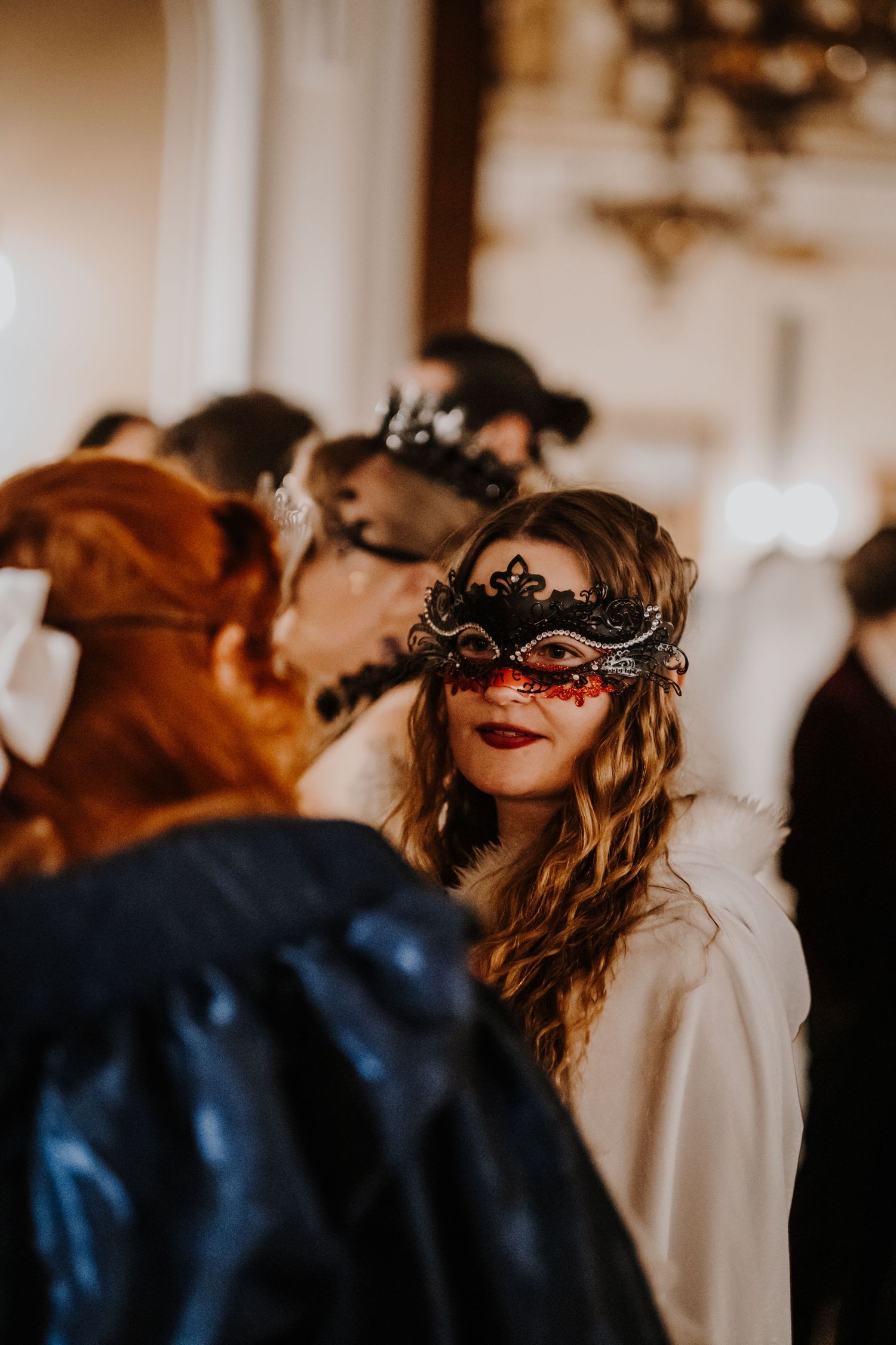 Attendees in dark masquerade masks and formal wear at an elegant ball.