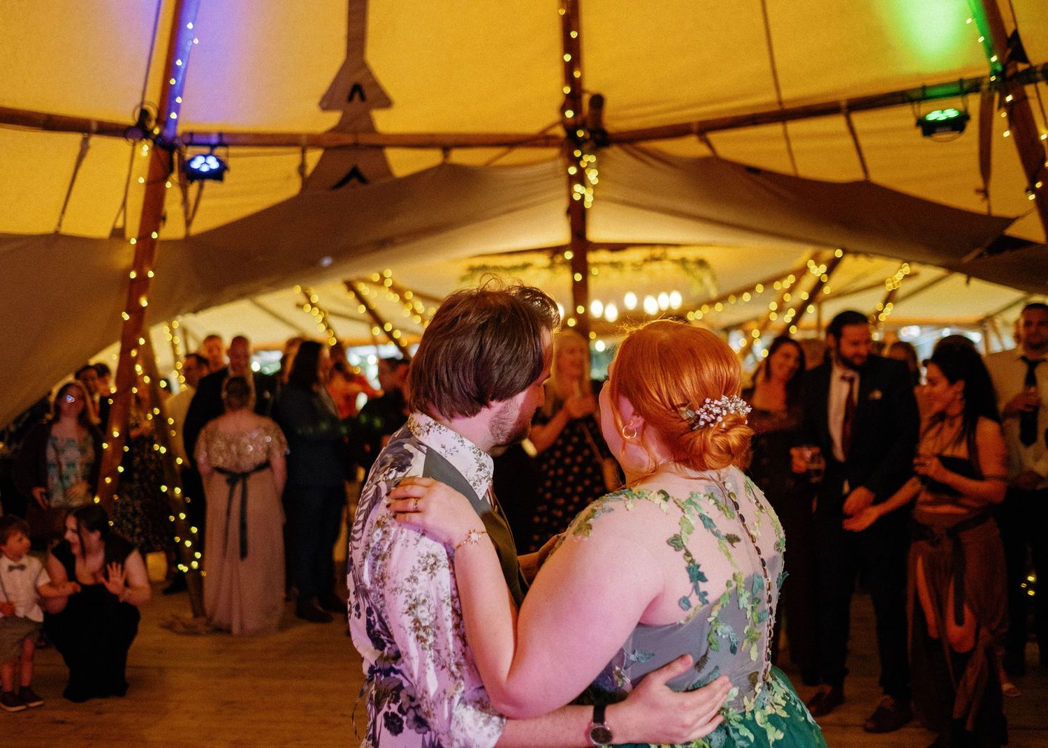Wedding reception dance under warm lighting in a tent with guests watching.
