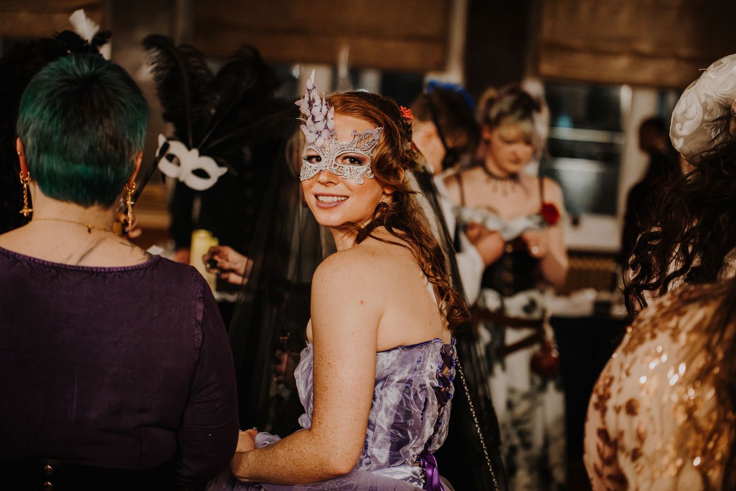 Guests wearing masks and formal attire mingle at an elegant indoor masquerade fantasy ball.