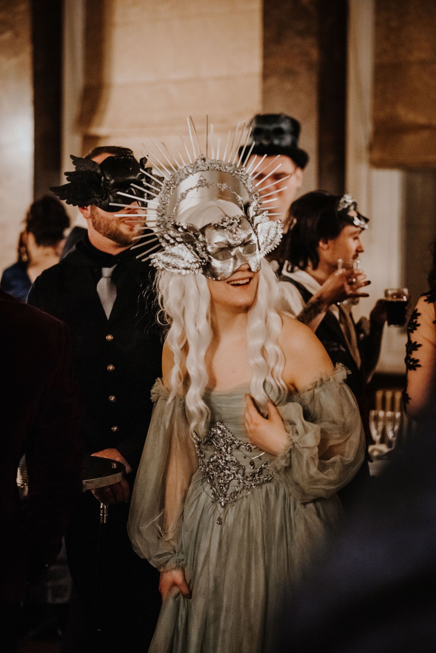 Masked figures wearing dramatic spiked headpieces at elegant evening event.