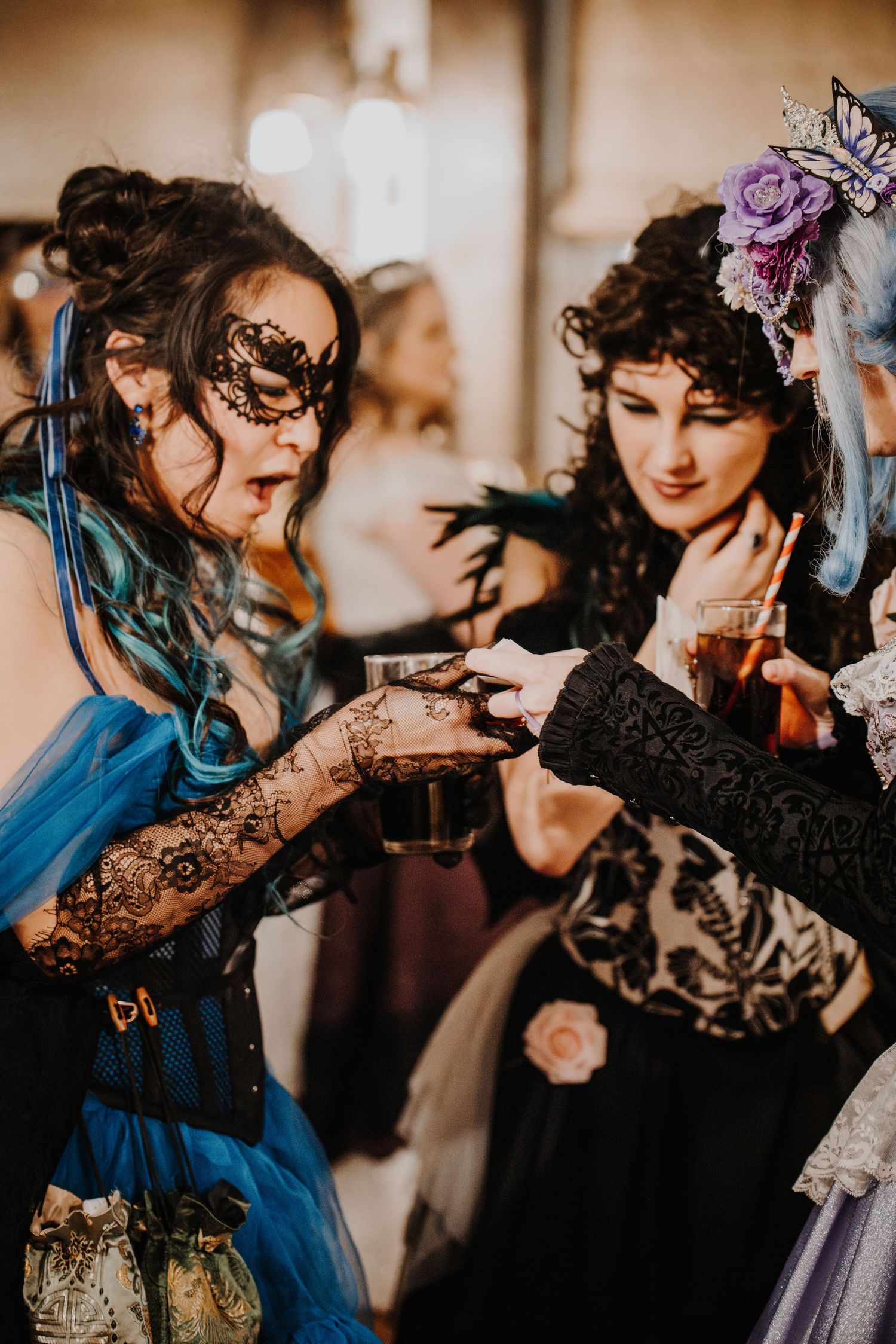 Guests in vintage-inspired dresses and masks pose together at a fantasy ball.