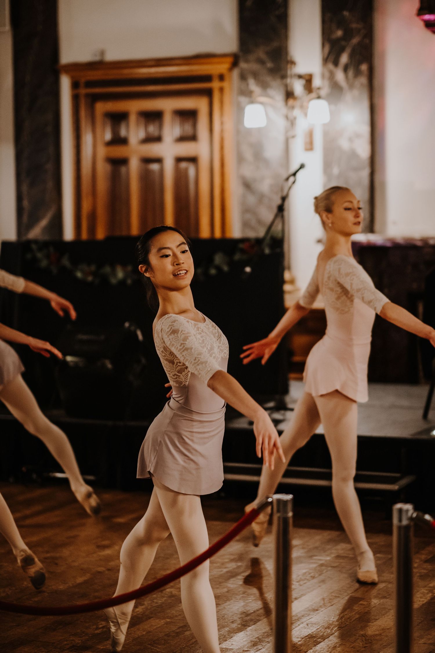Ballet dancers in white practice poses in classical dance studio.