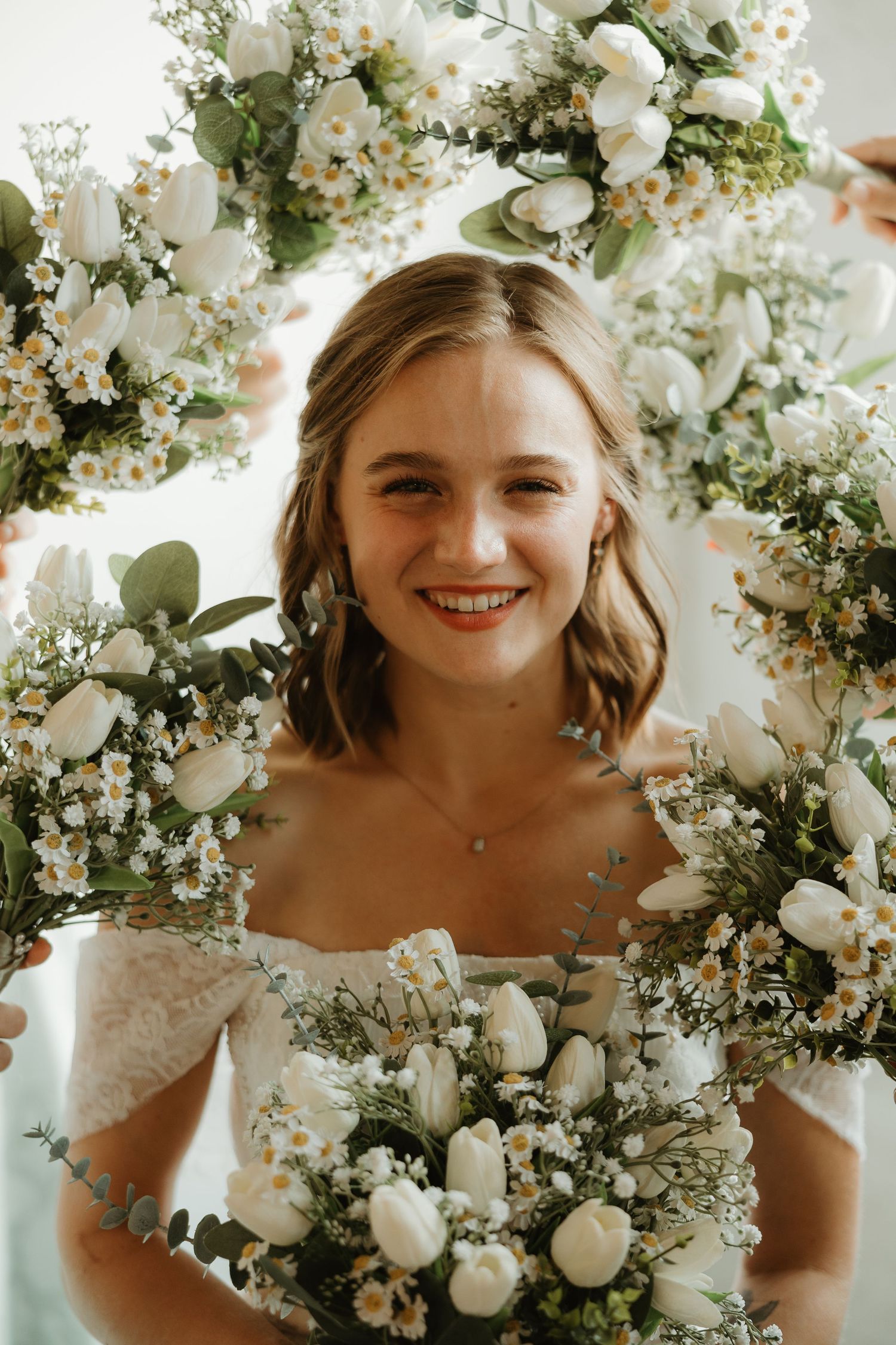 A beautiful bridal portrait surrounded by white floral arrangements and greenery in a soft, warm light setting.