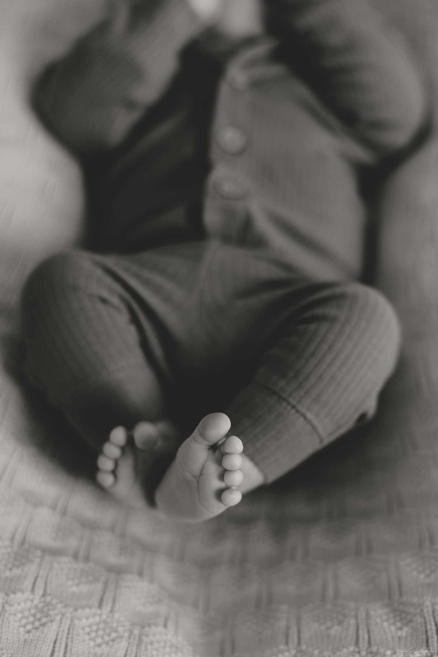 Black and white close-up of tiny bare feet resting on a textured floor.