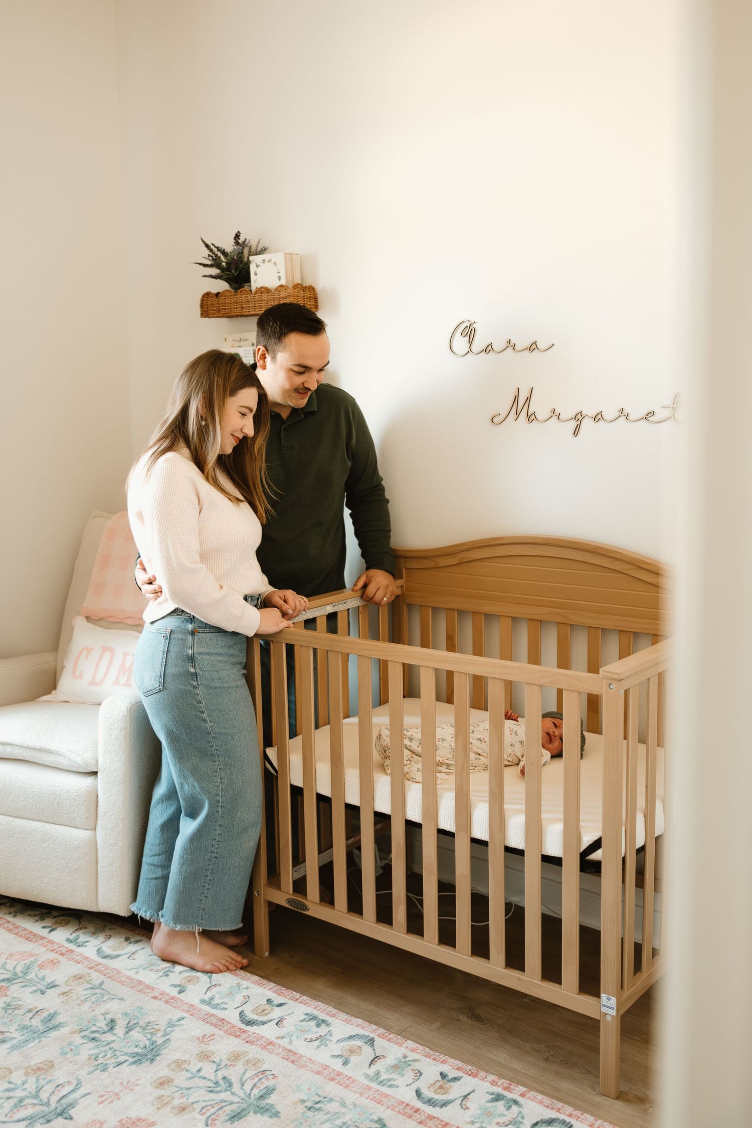 Couple assembles wooden crib in nursery with floral rug and white walls for their expected baby.
