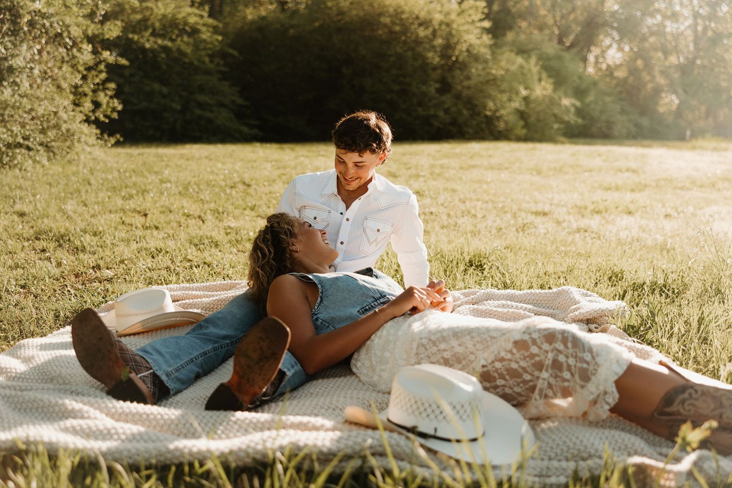 A couple lounges on a picnic blanket in a sunlit meadow during a romantic afternoon date in summer.