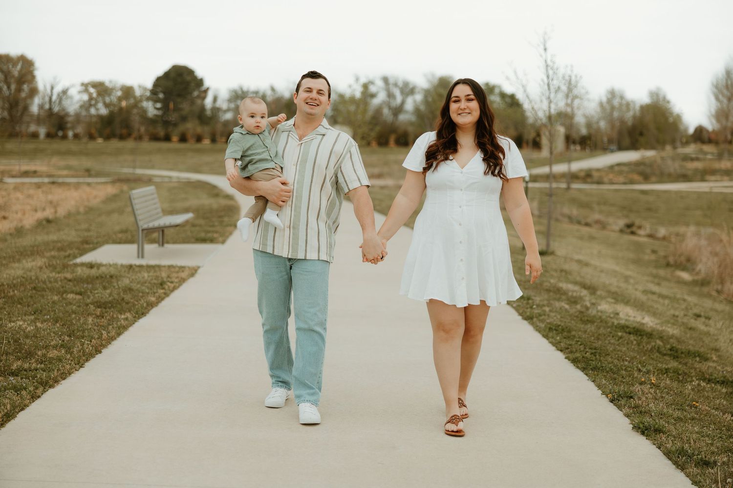 Couple walks together on concrete path through grassy field on warm spring day.