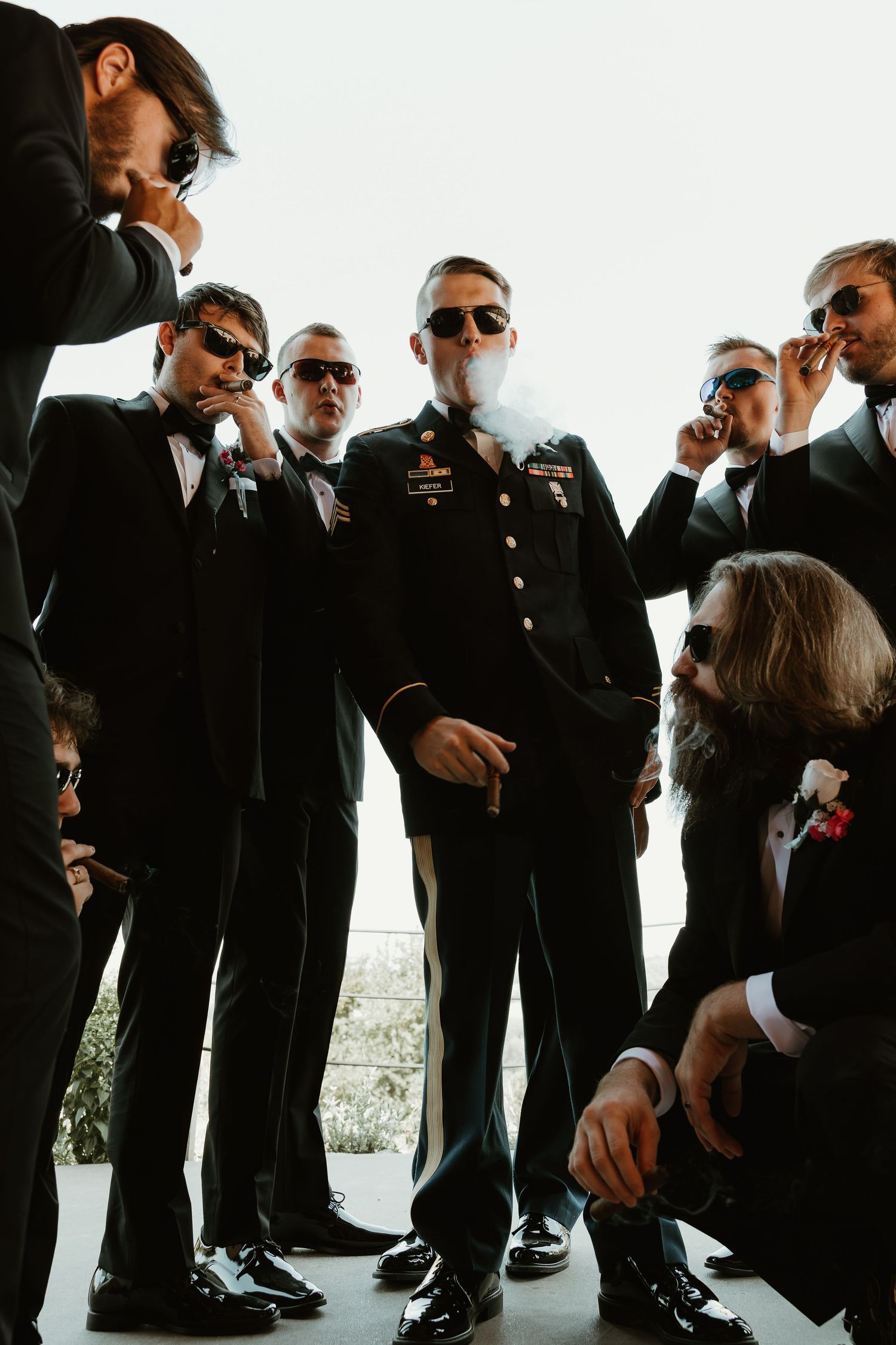 A group of people wearing black suits and sunglasses pose together in a stylish wedding party photo.