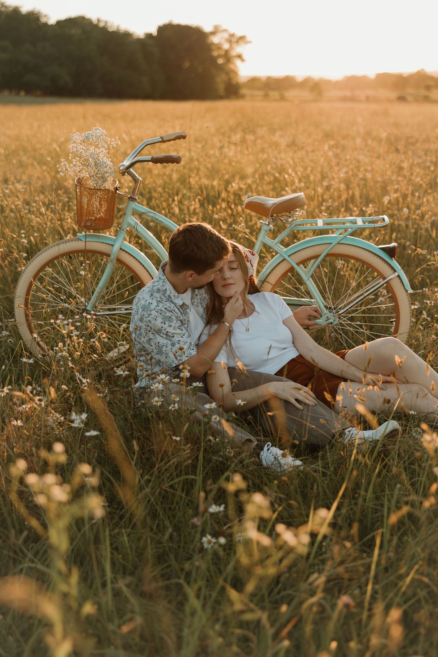 A couple enjoys an intimate moment in a golden field at sunset next to a mint green vintage bicycle.