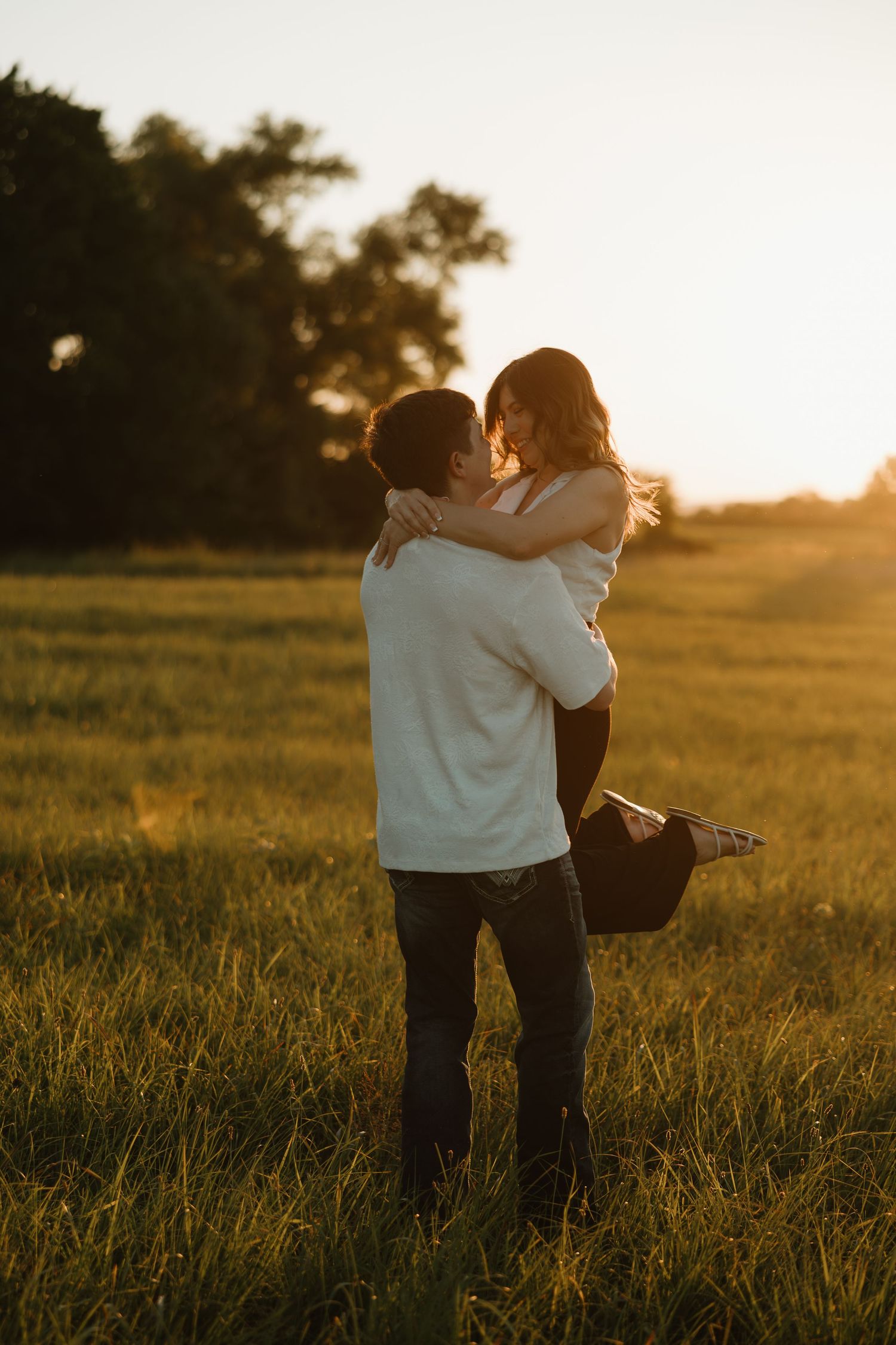 A couple embraces in a serene field at golden hour while the sun sets behind them creating a warm silhouette.
