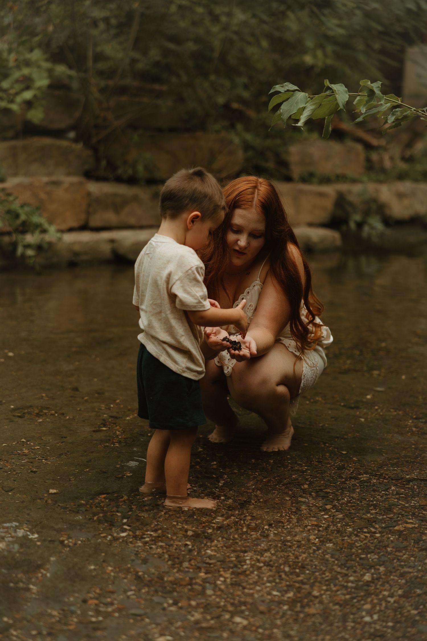 A tender moment shared between parent and child exploring together by a rocky riverbank in nature.