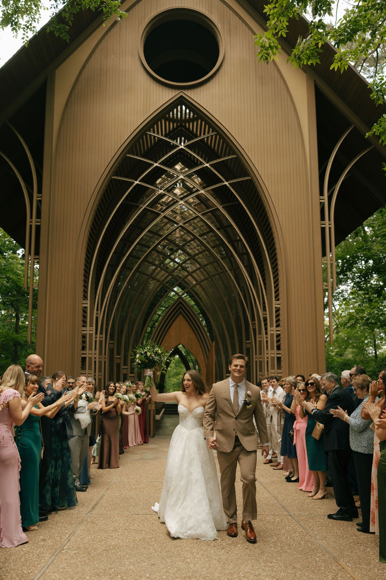 Bride and groom exit gothic chapel arch surrounded by cheering wedding guests lining the path.