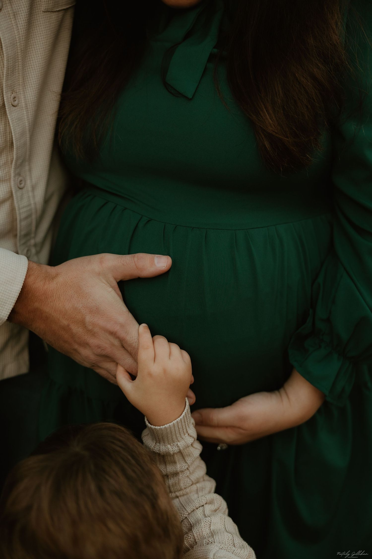 Tender moment with hands touching a green maternity dress against dark background.