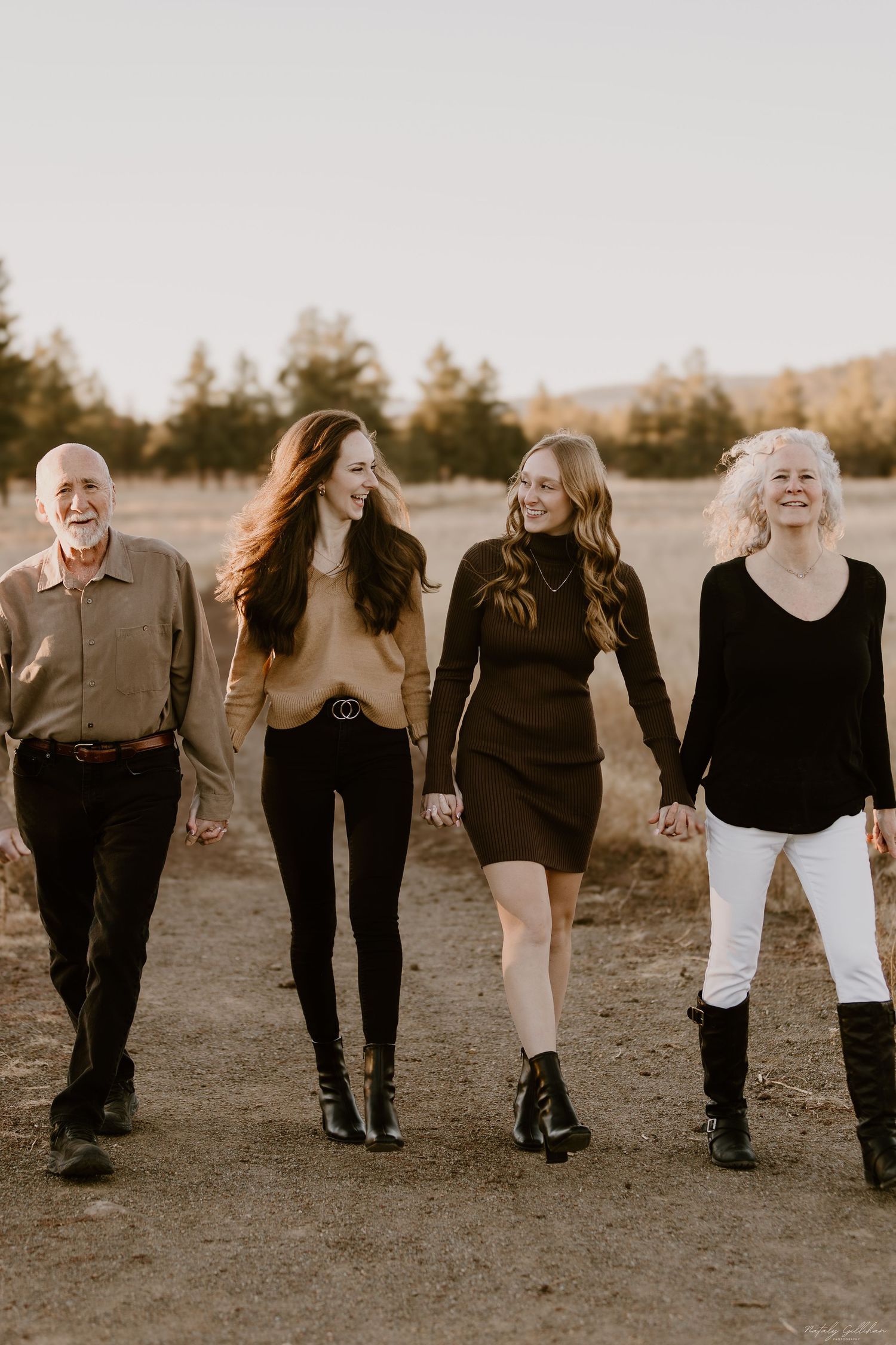 Four family members walk together outdoors at sunset while wearing contrasting black and light-colored outfits.