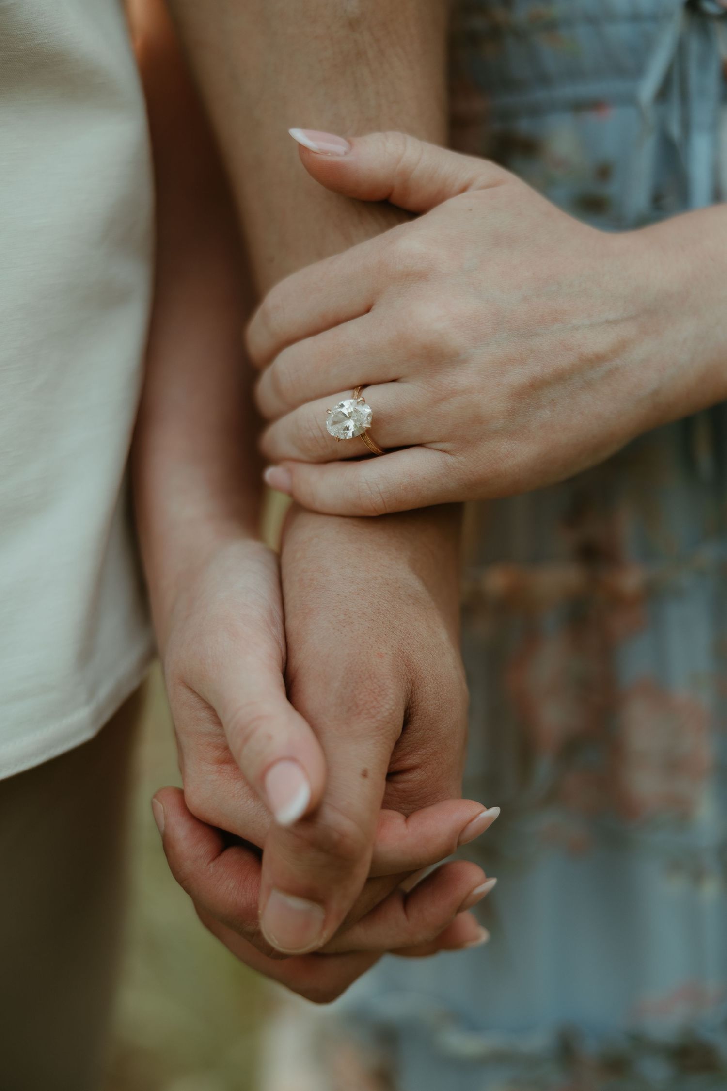 A close-up shot of two hands clasped together with a diamond engagement ring visible on one hand.