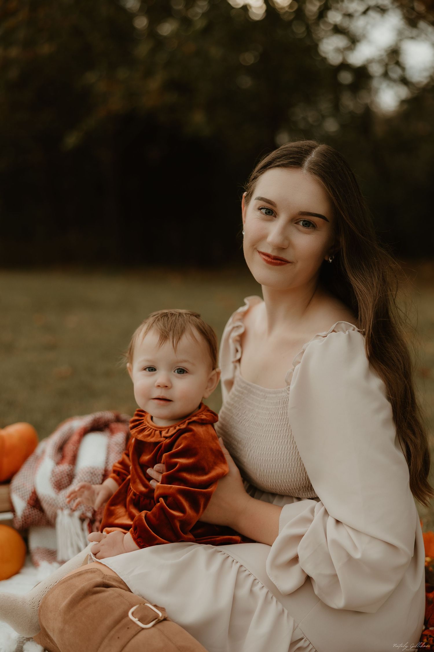 A fall-themed outdoor portrait features a white dress and small child in orange velvet amid pumpkins and blankets.