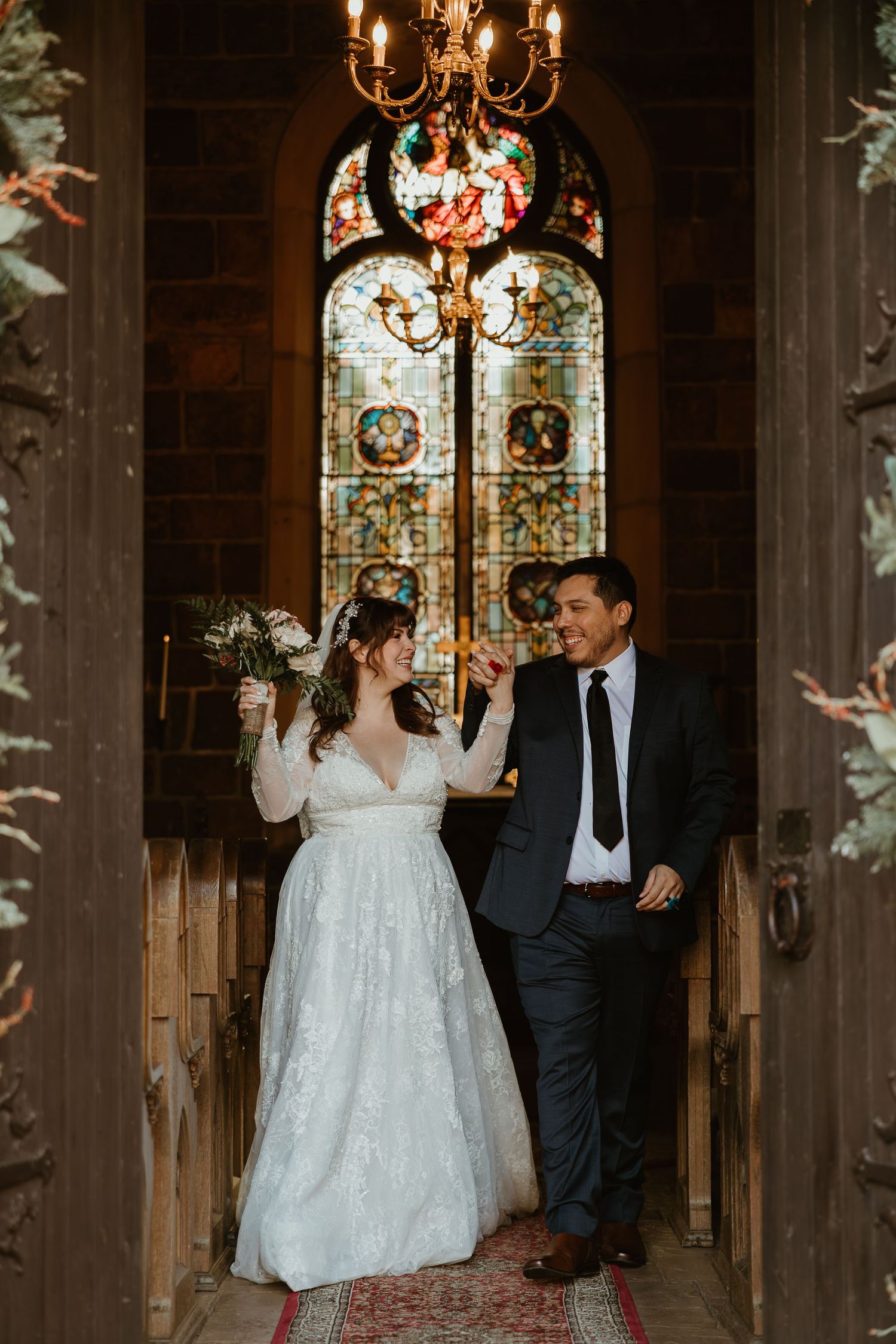 A couple shares a joyful moment in a church with stained glass windows and candlelit chandeliers.