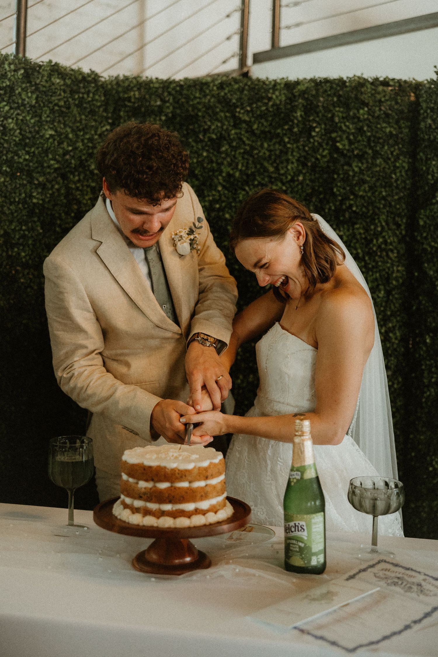 Couple cutting into their simple two-tier naked wedding cake during an intimate outdoor reception celebration.