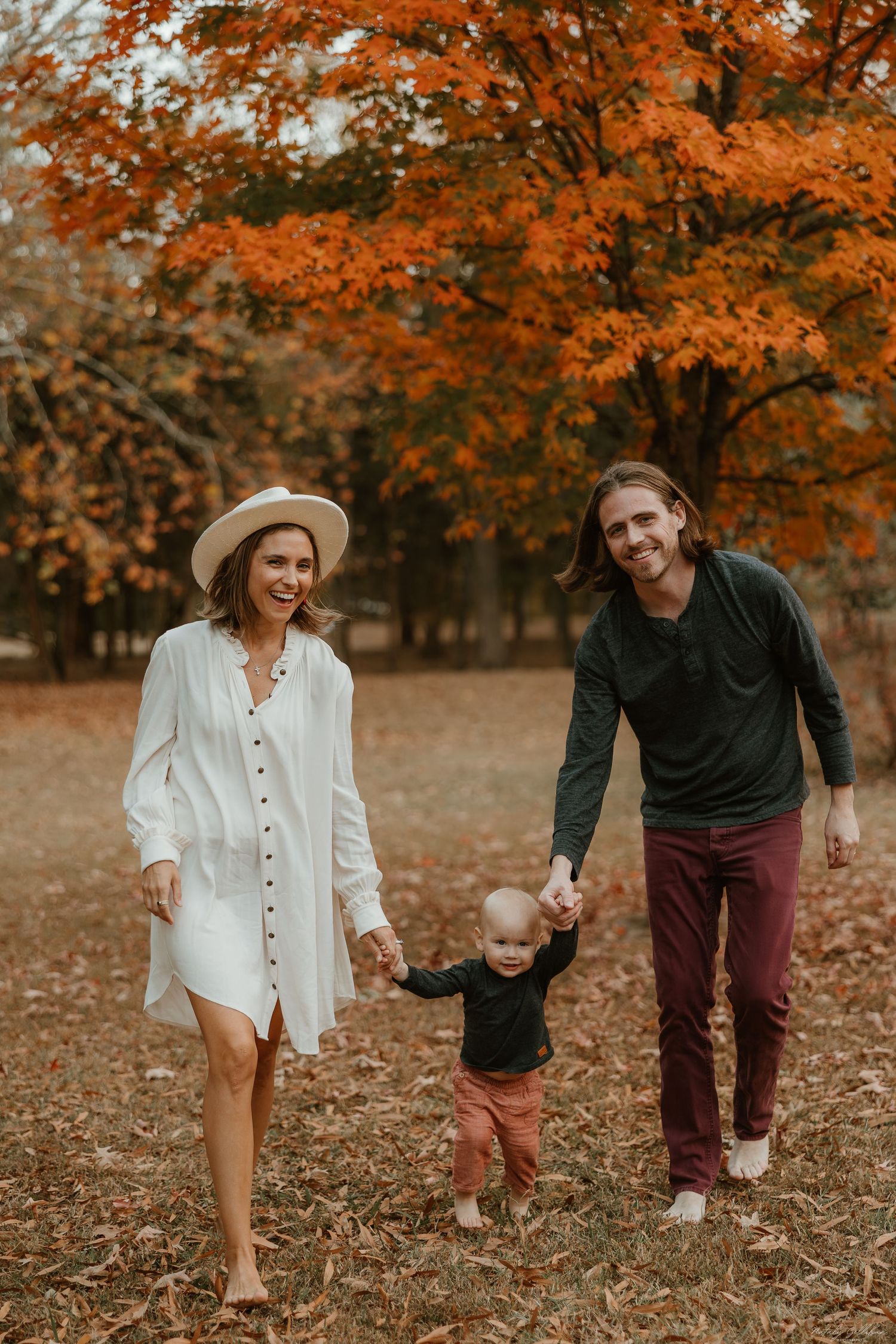 Family walking through autumn leaves in coordinated outfits with vibrant orange foliage overhead.