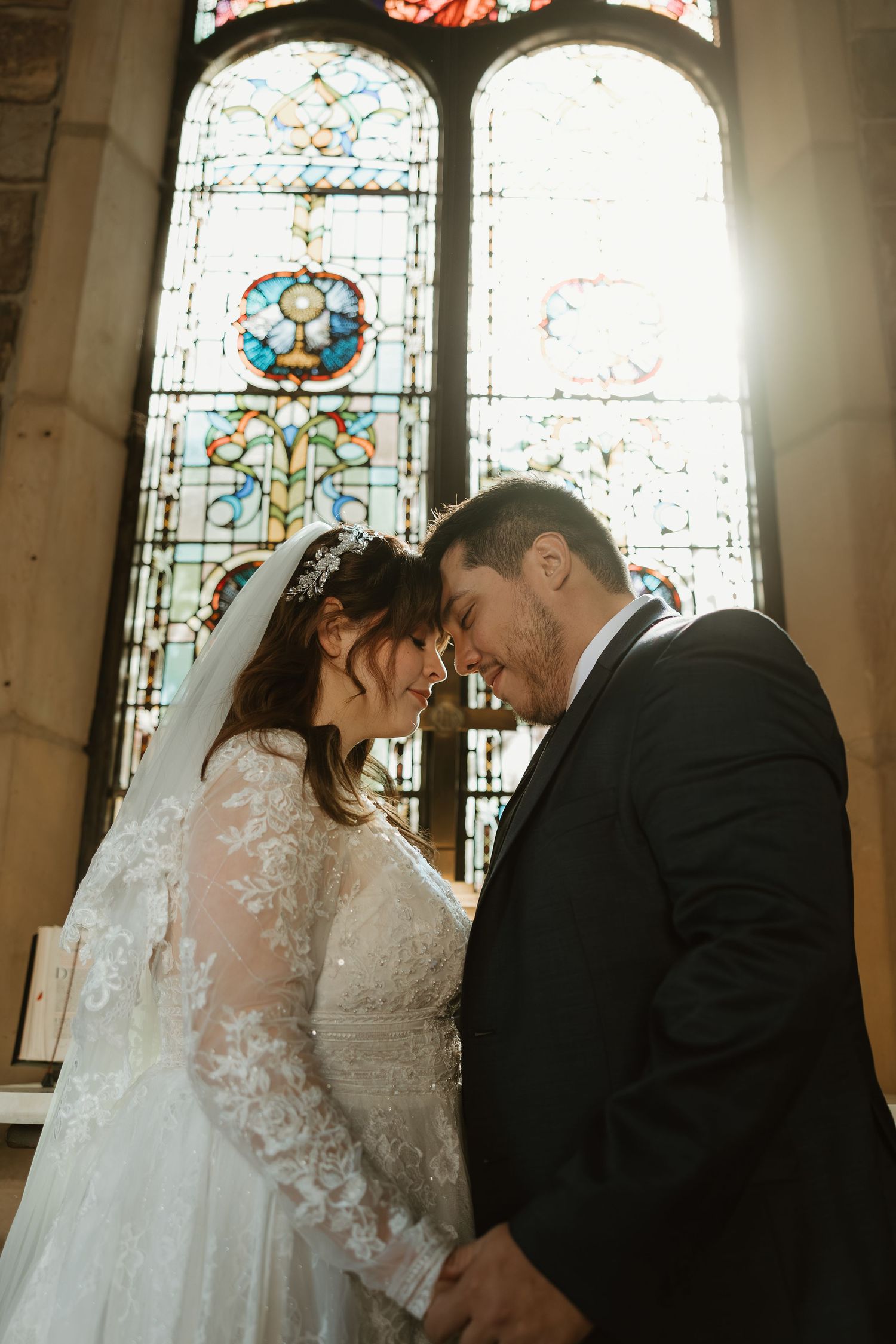 A romantic moment between newlyweds in a church with beautiful stained glass windows in the background.