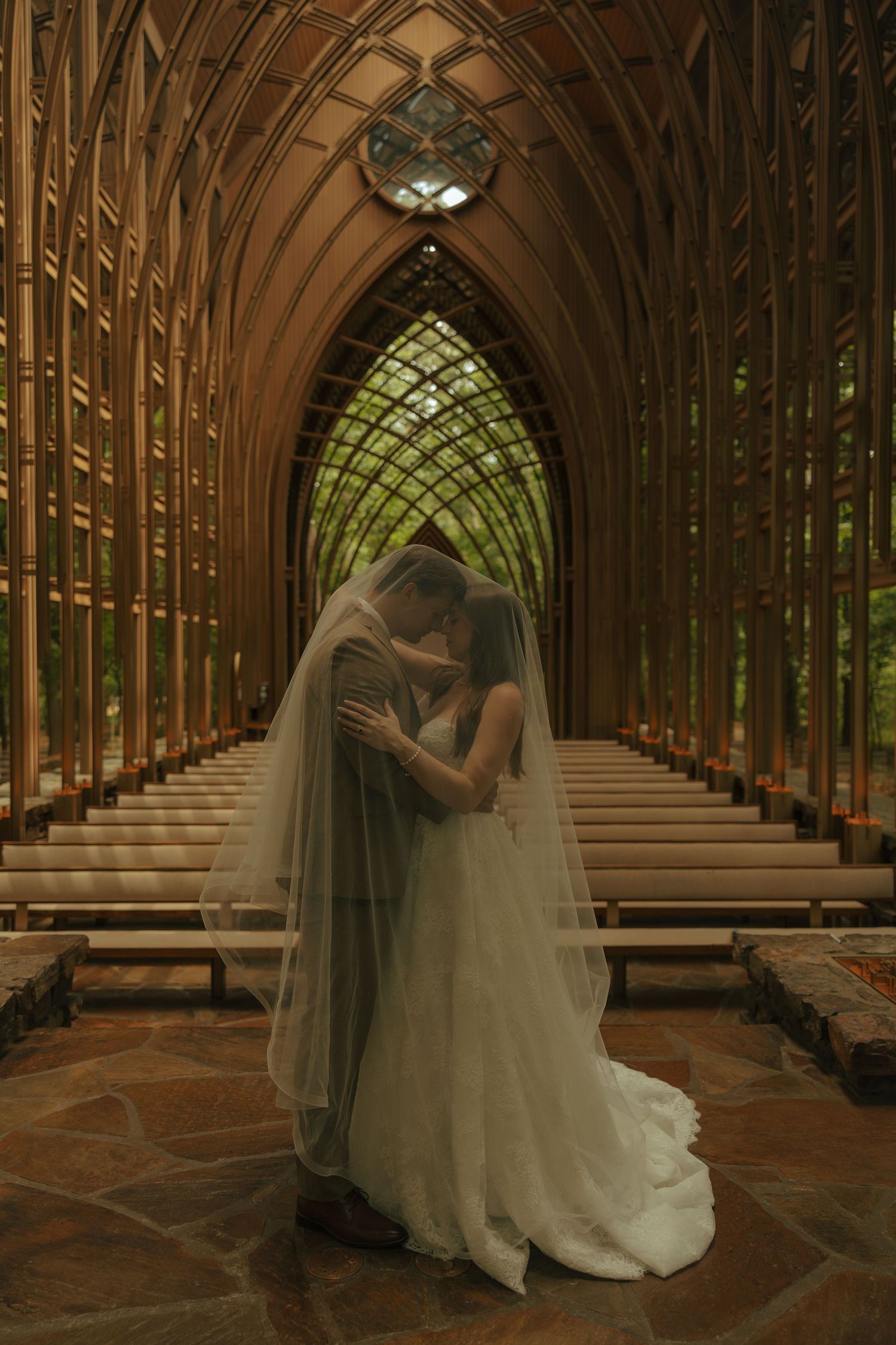 Bride and groom share an intimate kiss under a flowing veil inside a stunning Gothic chapel with arched wooden beams.