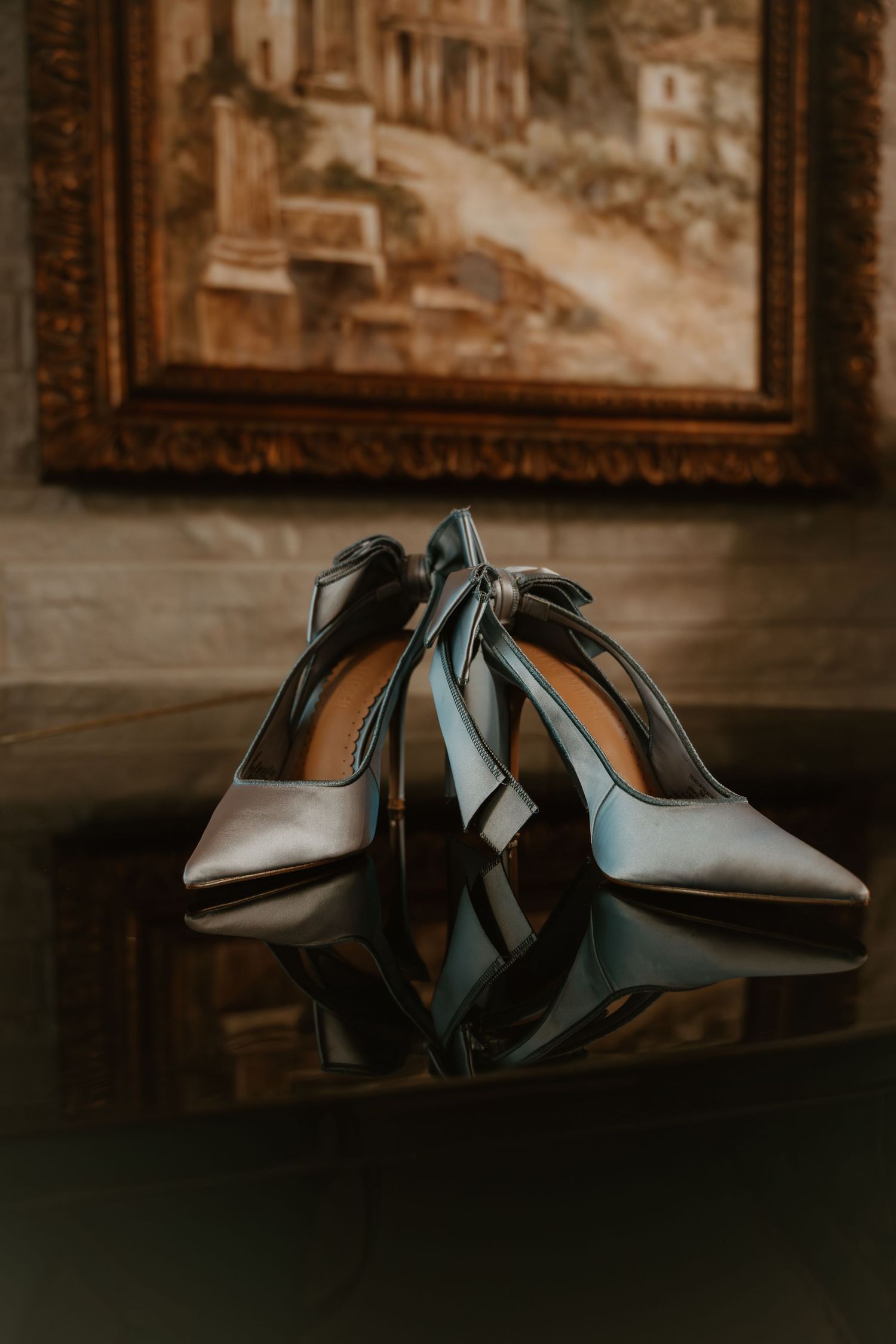 Elegant silver high heel shoes arranged artistically in a moody dark setting with framed artwork in the background.