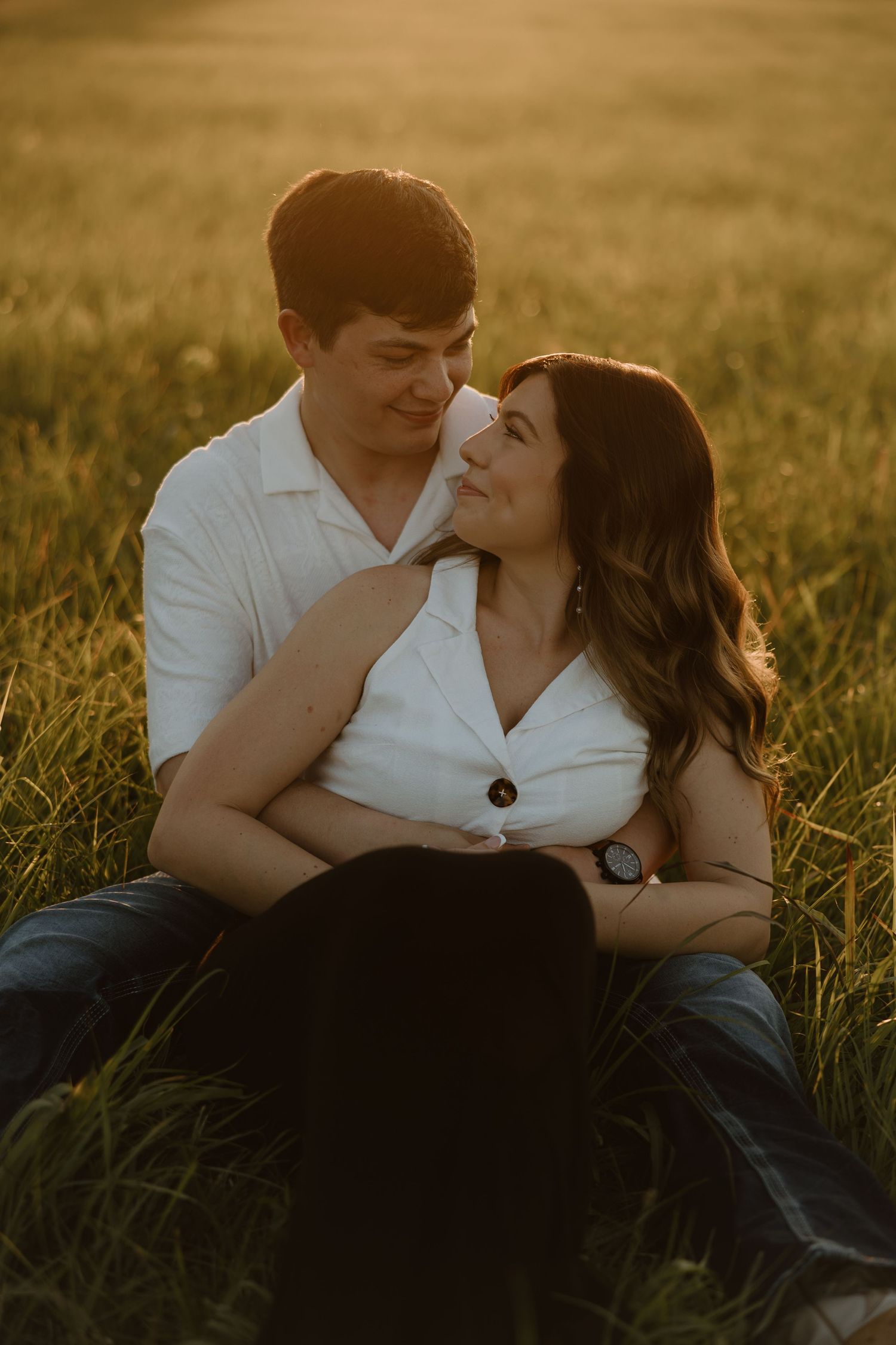 Romantic couple relaxing in golden sunlit meadow during sunset photoshoot.