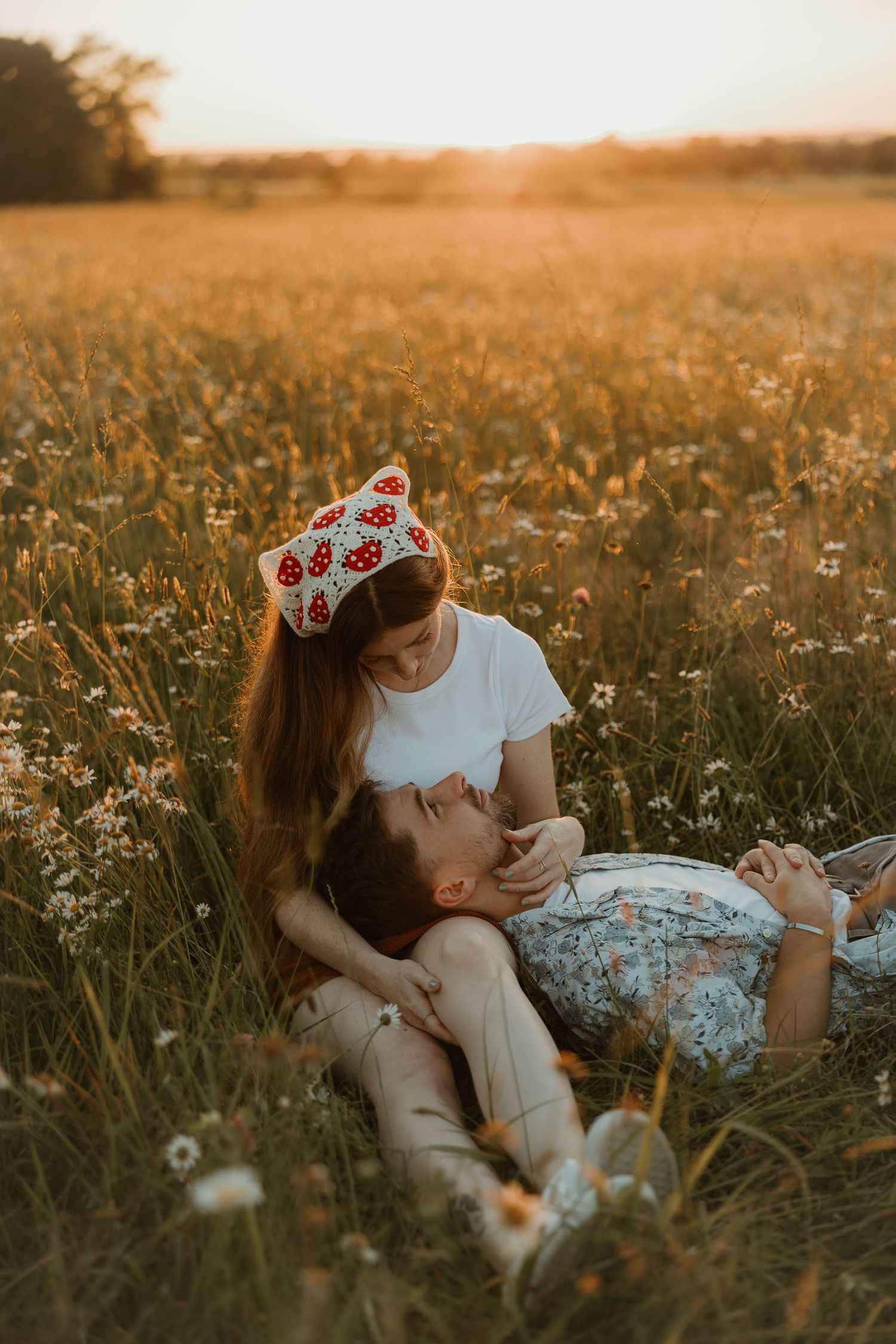 Couple lying in a dreamy summer meadow with wildflowers during golden hour sunset.