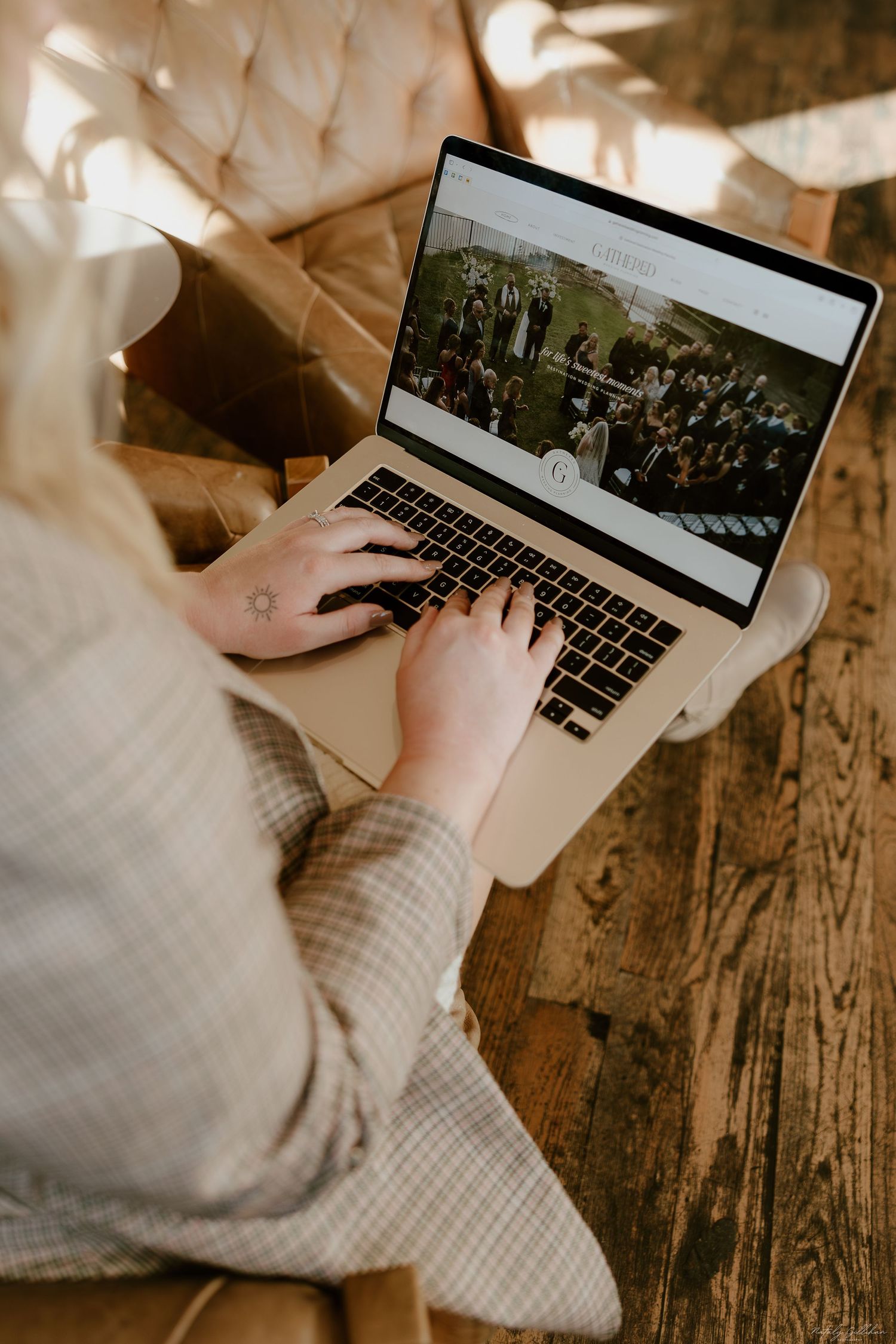 Hands type on a laptop keyboard displaying a crowd photo while sitting on a rustic wooden floor.