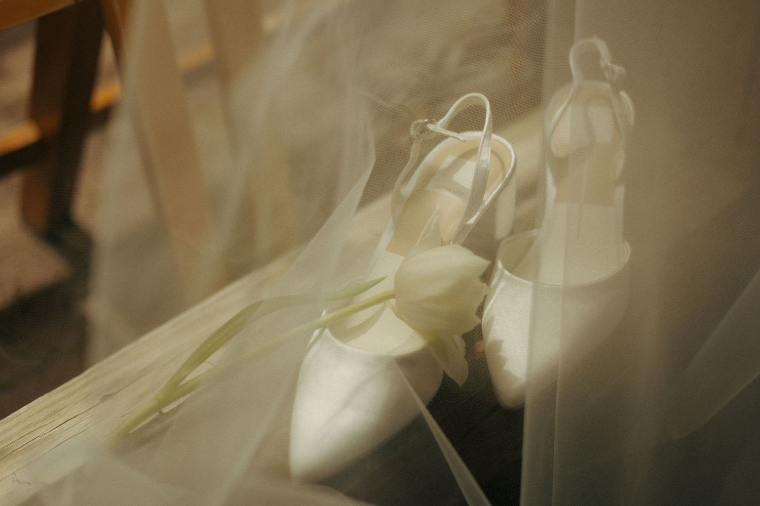 Elegant white bridal heels with slingback straps and a calla lily resting on a sheer wedding veil.