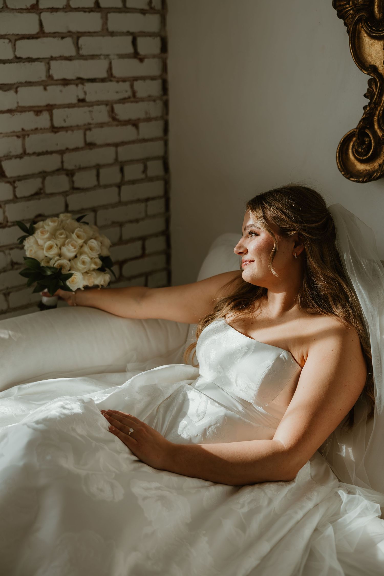 Artistic boudoir photography series showing a figure draped in white sheets against exposed brick wall.