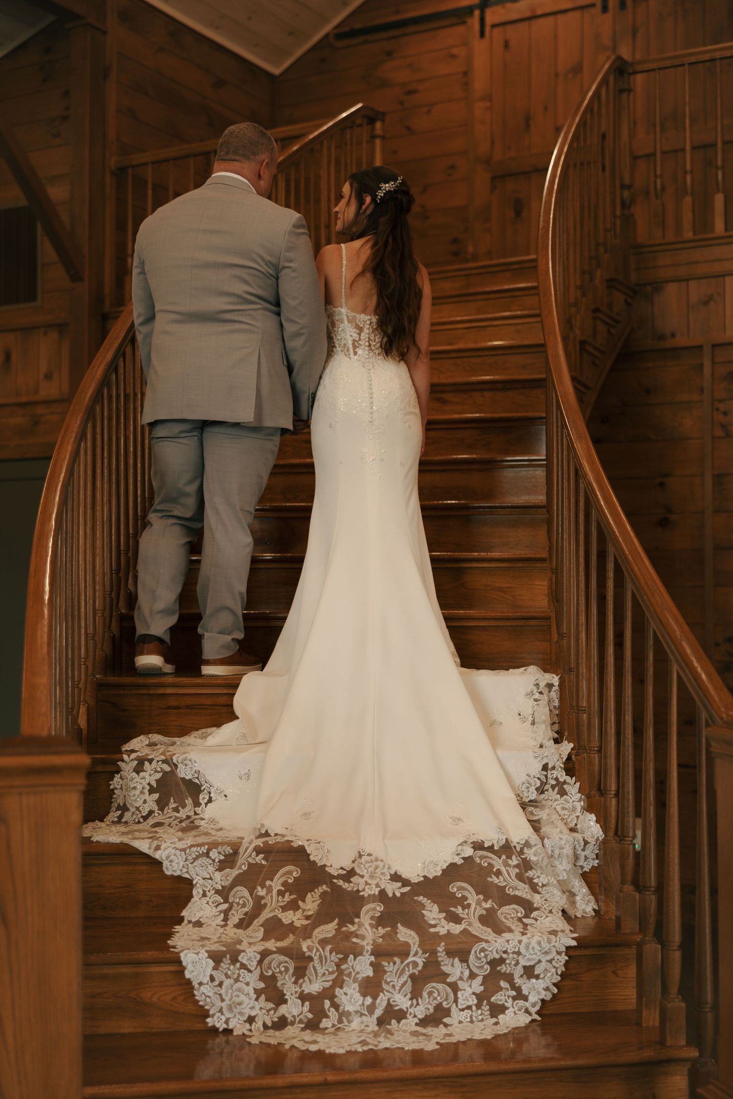 A couple stands on a wooden staircase with the bride wearing a stunning lace-trimmed mermaid wedding gown.