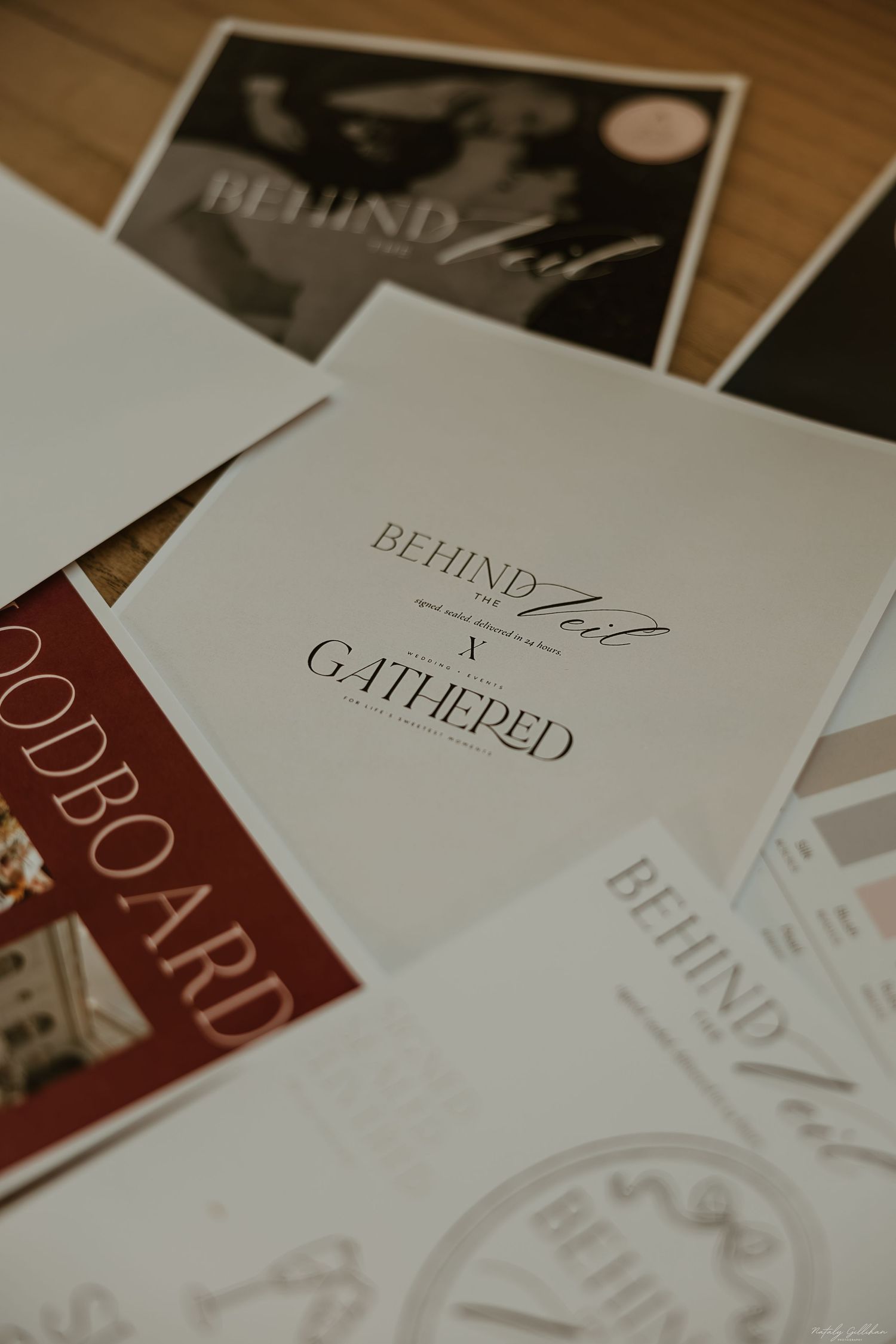 Close-up view of printed materials featuring 'BEHIND' and 'GALLIED' text on white papers laid on wooden surface.