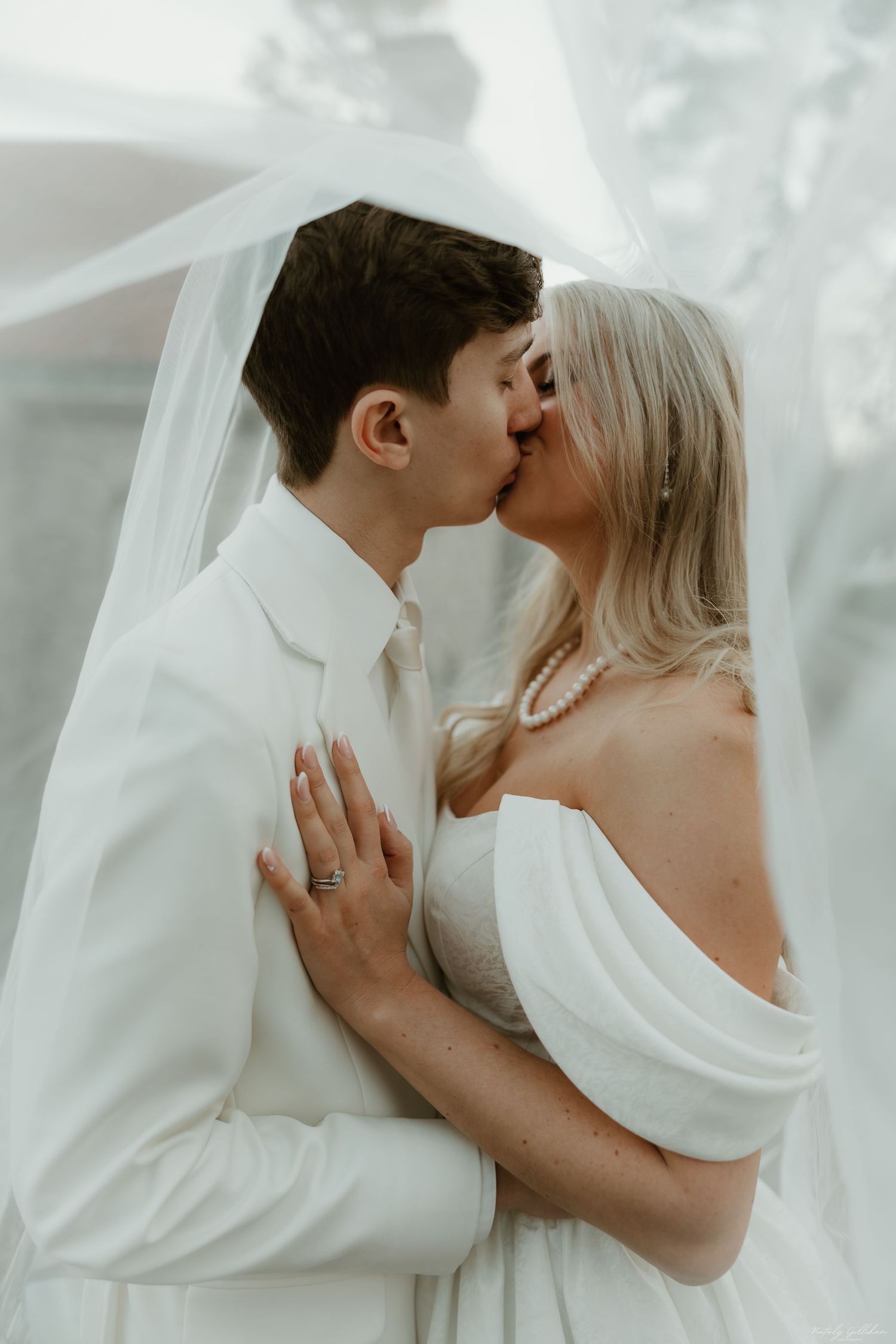 A romantic wedding moment captured in soft muted tones as a couple shares an intimate kiss.