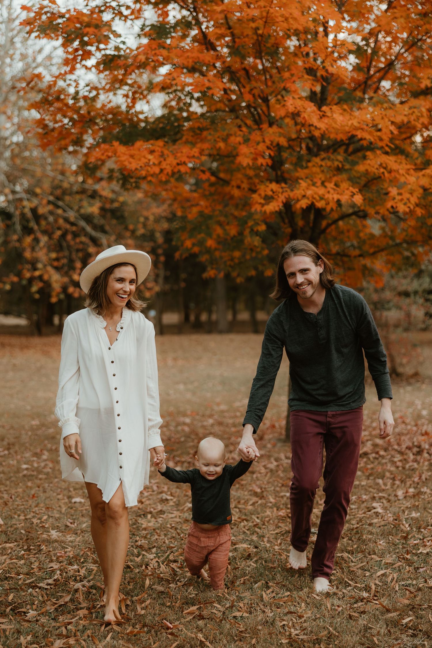A family walking together through fallen autumn leaves under vibrant orange maple trees in a park setting.