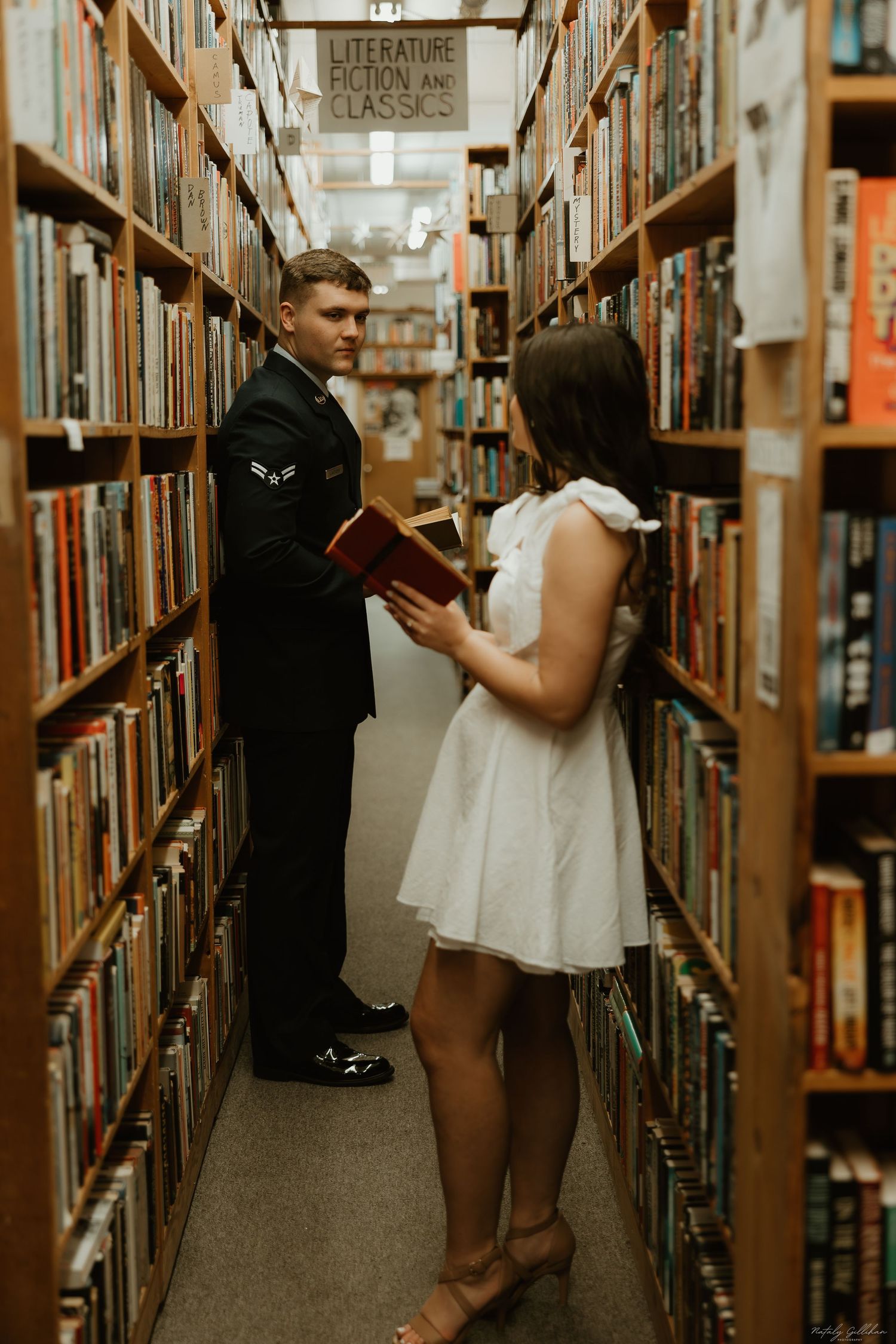 A couple in formal attire shares a romantic moment between bookshelves in a library.