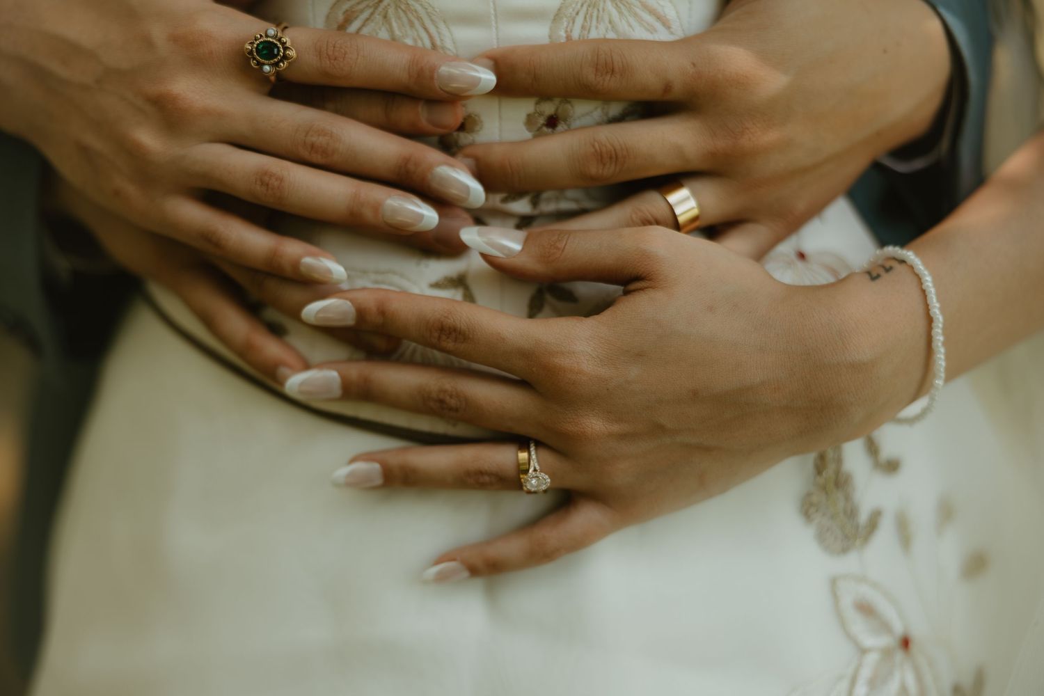 Close-up view of hands wearing engagement rings with delicate lace details in the background.