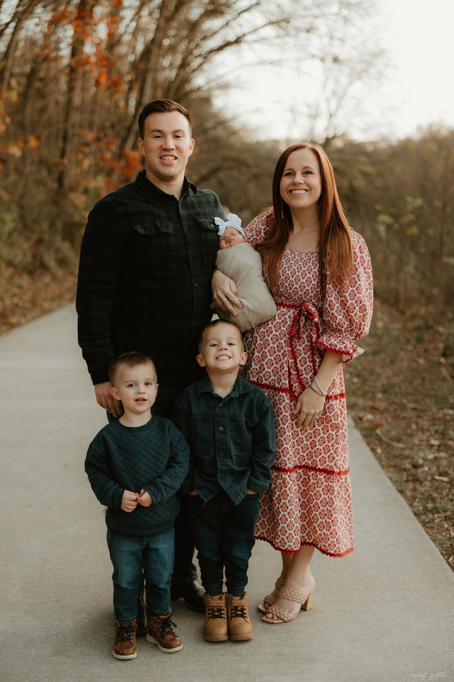 Family portrait on a paved path during autumn with coordinated outfits in navy and red.