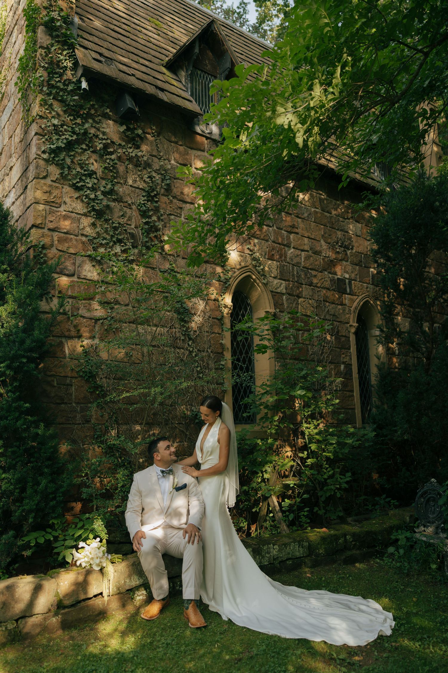 Bride and groom pose romantically outside an ivy-covered stone castle, surrounded by lush greenery on their wedding day.