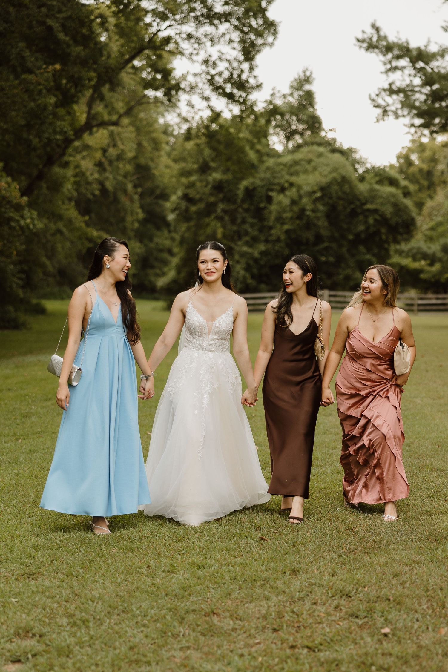A group in formal attire sits together on grass in coordinated blue, white, brown and rose-colored dresses.
