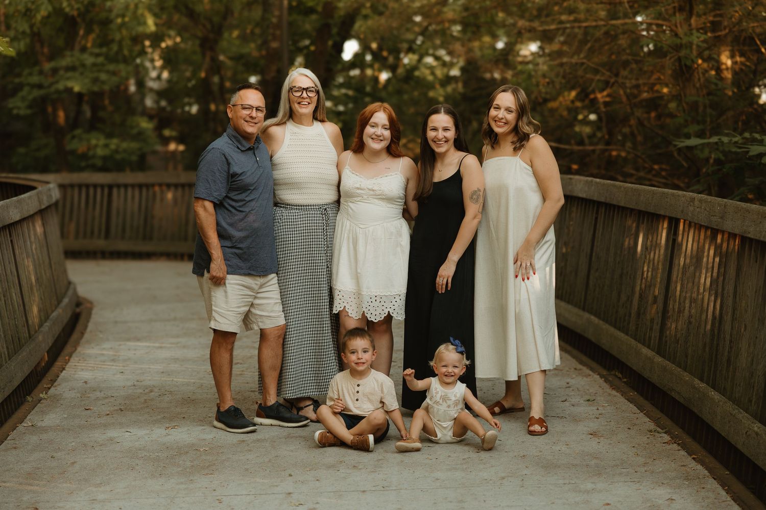 A group of people pose together on a wooden boardwalk surrounded by lush greenery in an outdoor setting.