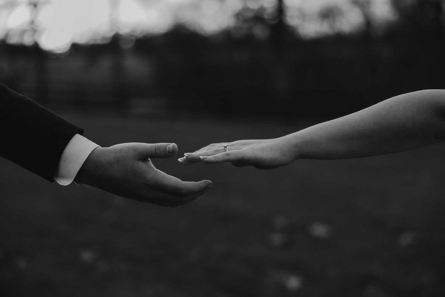 Black and white close-up photograph of hands reaching towards each other against a dark background.