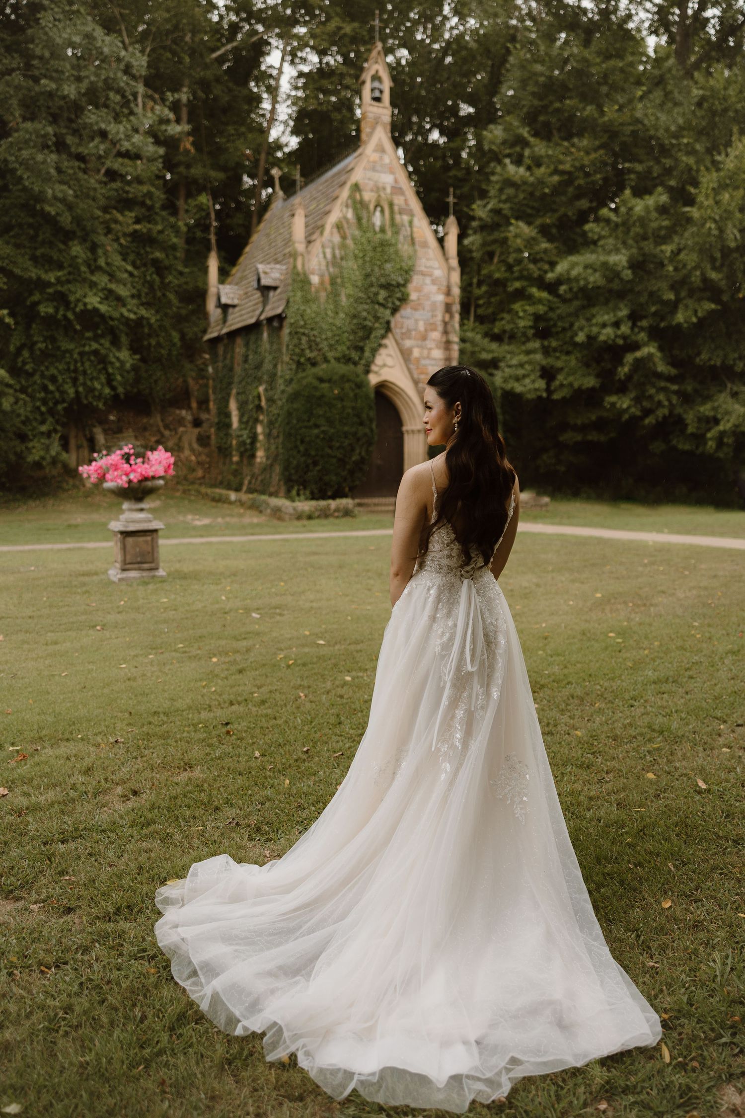 A flowing white wedding dress twirls gracefully on a grassy lawn with a stone church building visible in the background.
