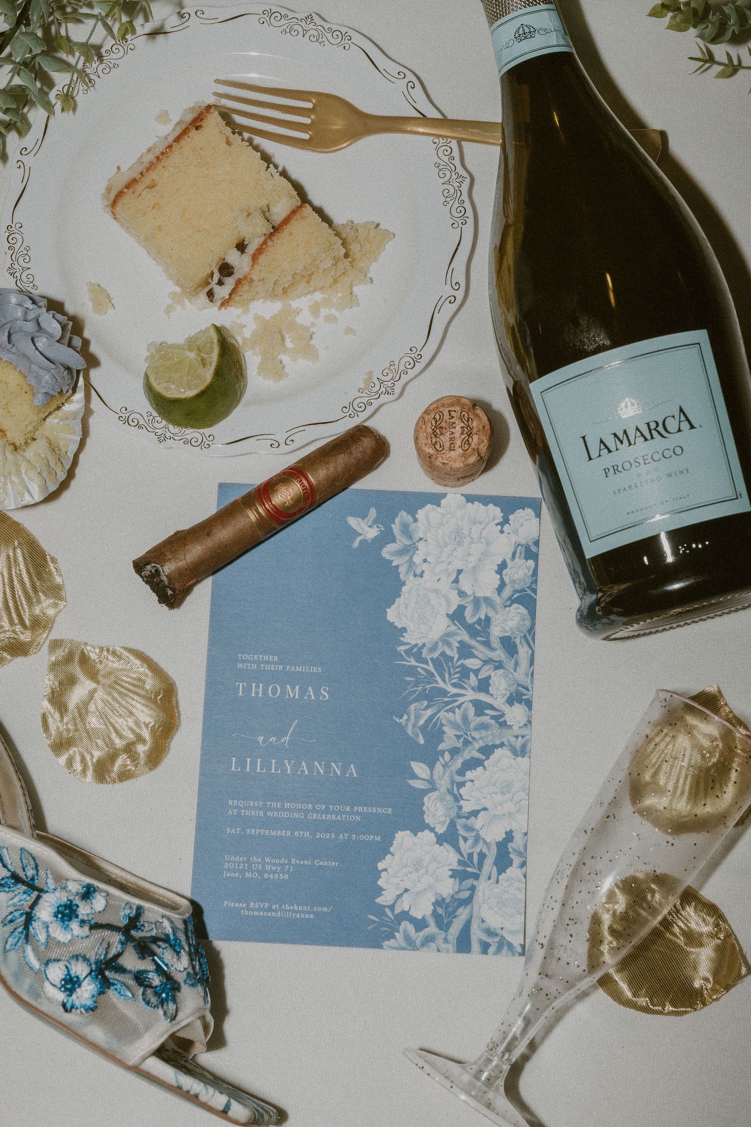 Wedding invitation cards and wine bottles arranged on a light surface with elegant blue and white design details.