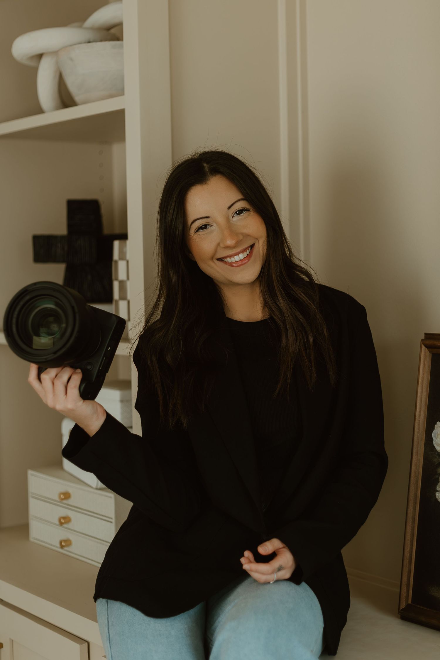A person in a black sweater sits casually smiling and laughing in a series of candid photos against a beige wall.