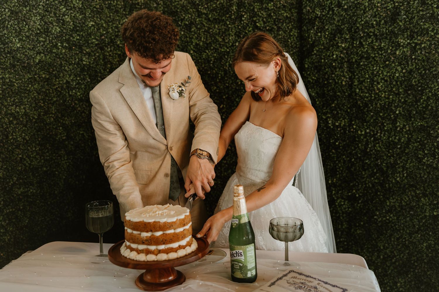 A couple shares an intimate moment while cutting their rustic naked wedding cake at an outdoor reception.