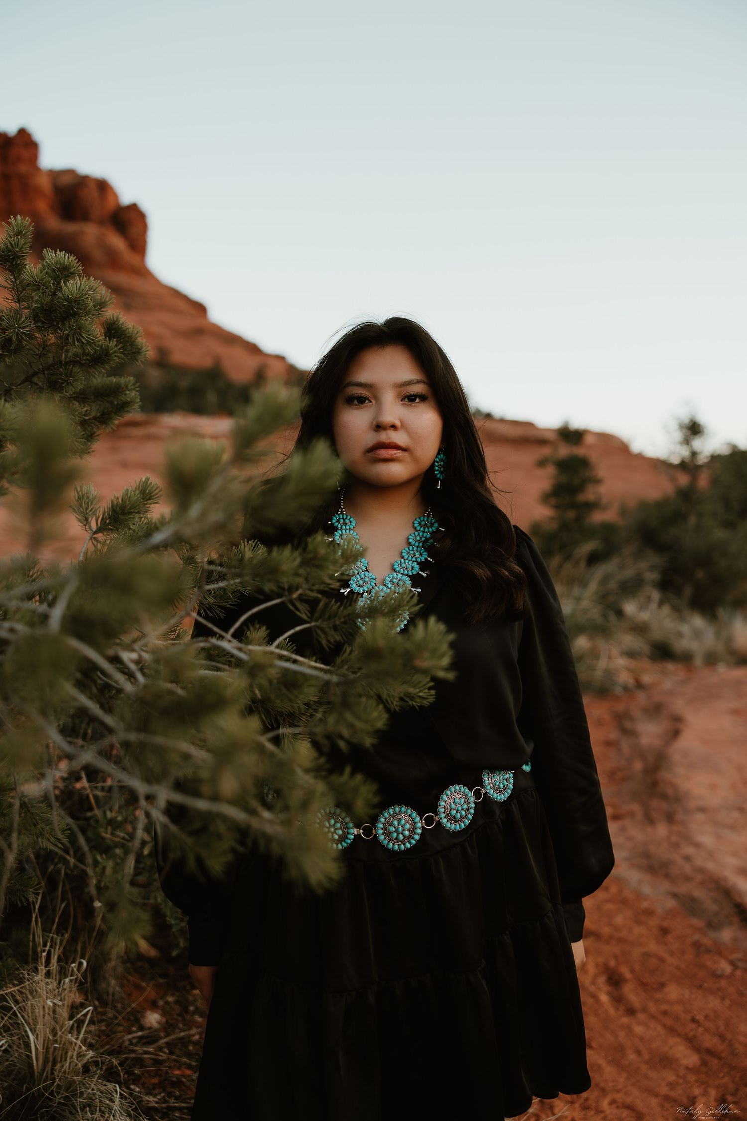 Beautiful traditional desert portrait featuring turquoise jewelry and a black velvet dress against red rock formations.